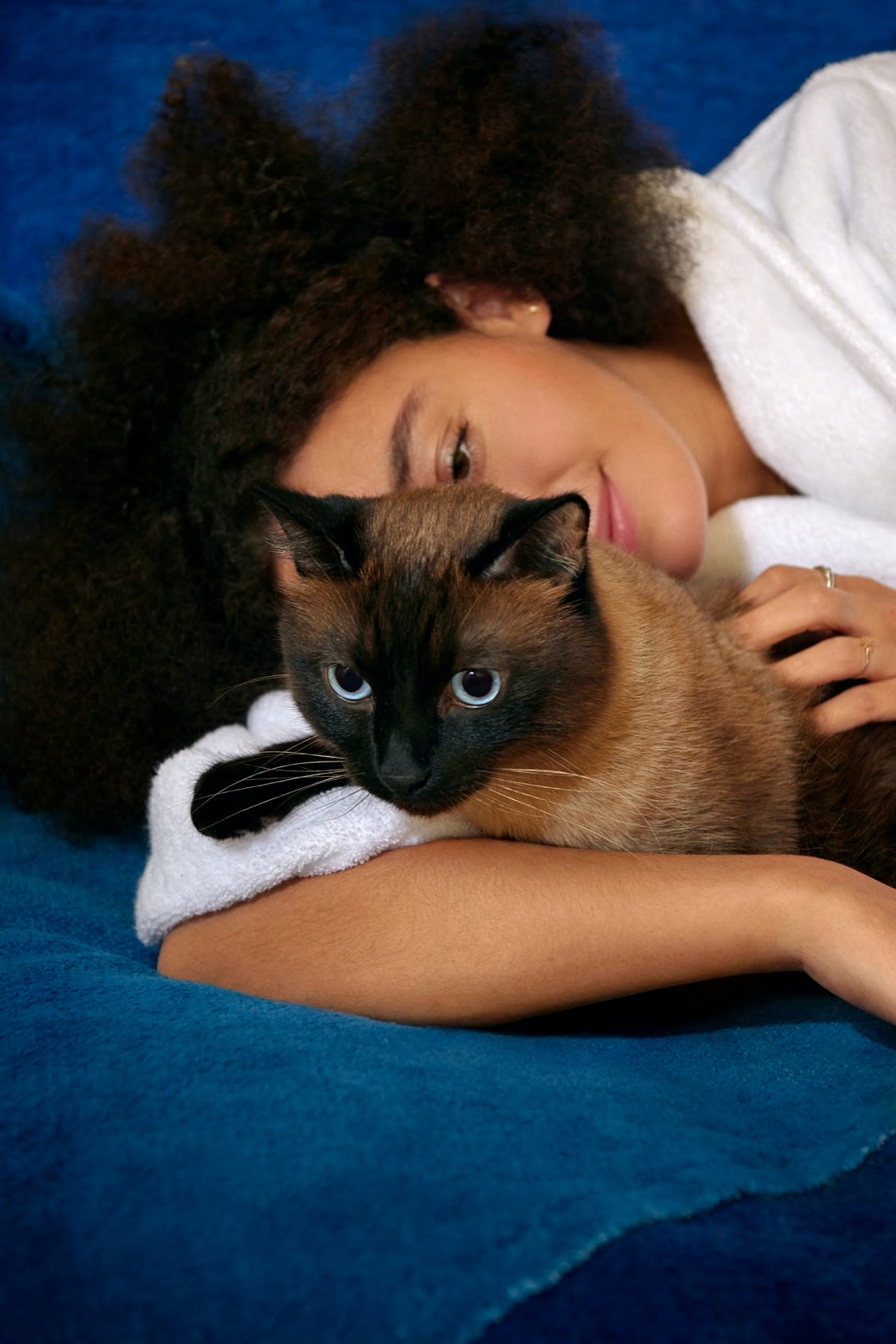 Woman in white bathrobe holding and petting her Siamese cat