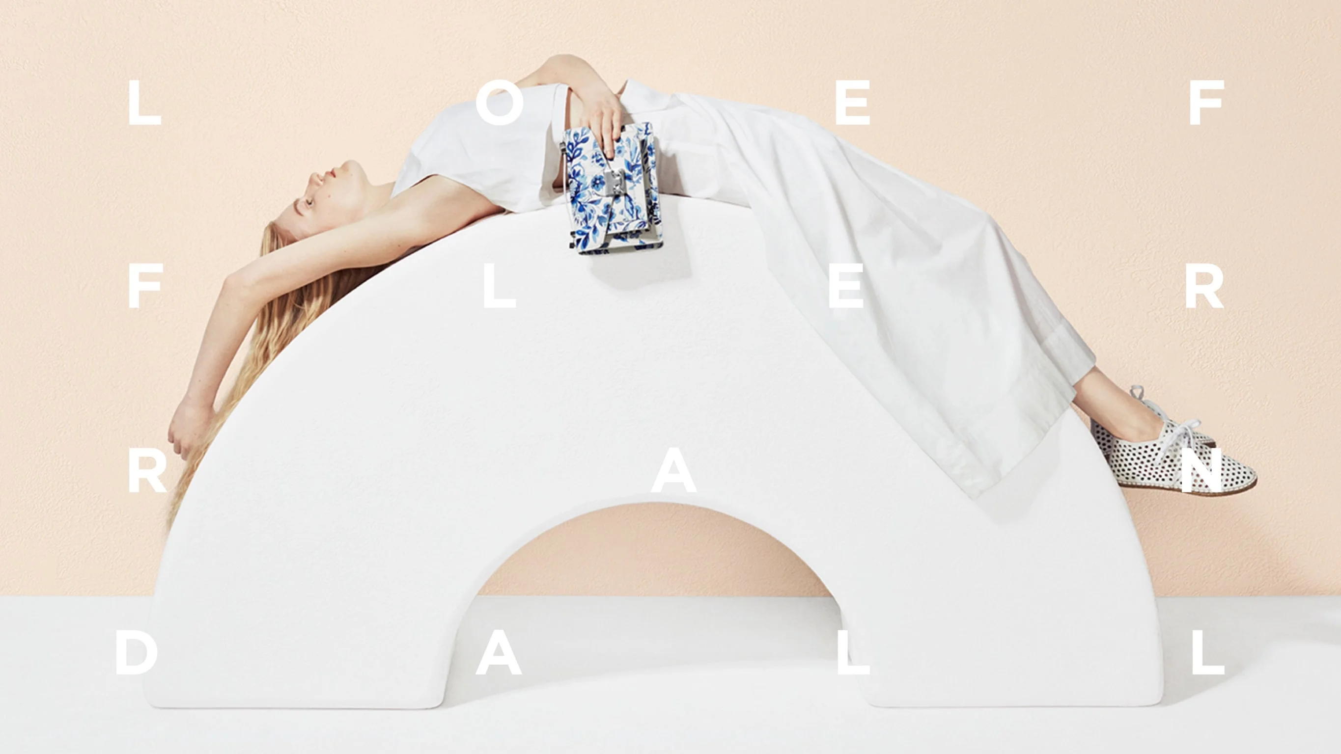 Loeffler Randall ad featuring model laying on white arch wearing white sneakers and holding blue embroidered pouch. Branding and Art direction by RoAndCo