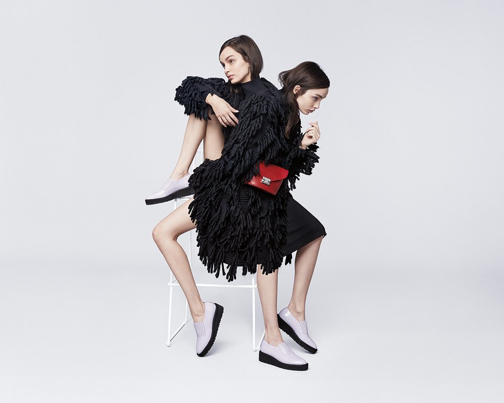 Two models leaning on a stool. Purple Loeffler Randall loafers and red envelope purse. Art Direction by RoAndCo