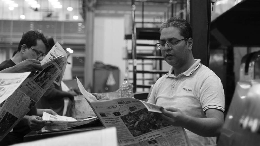 Two people reading newspapers in a print room