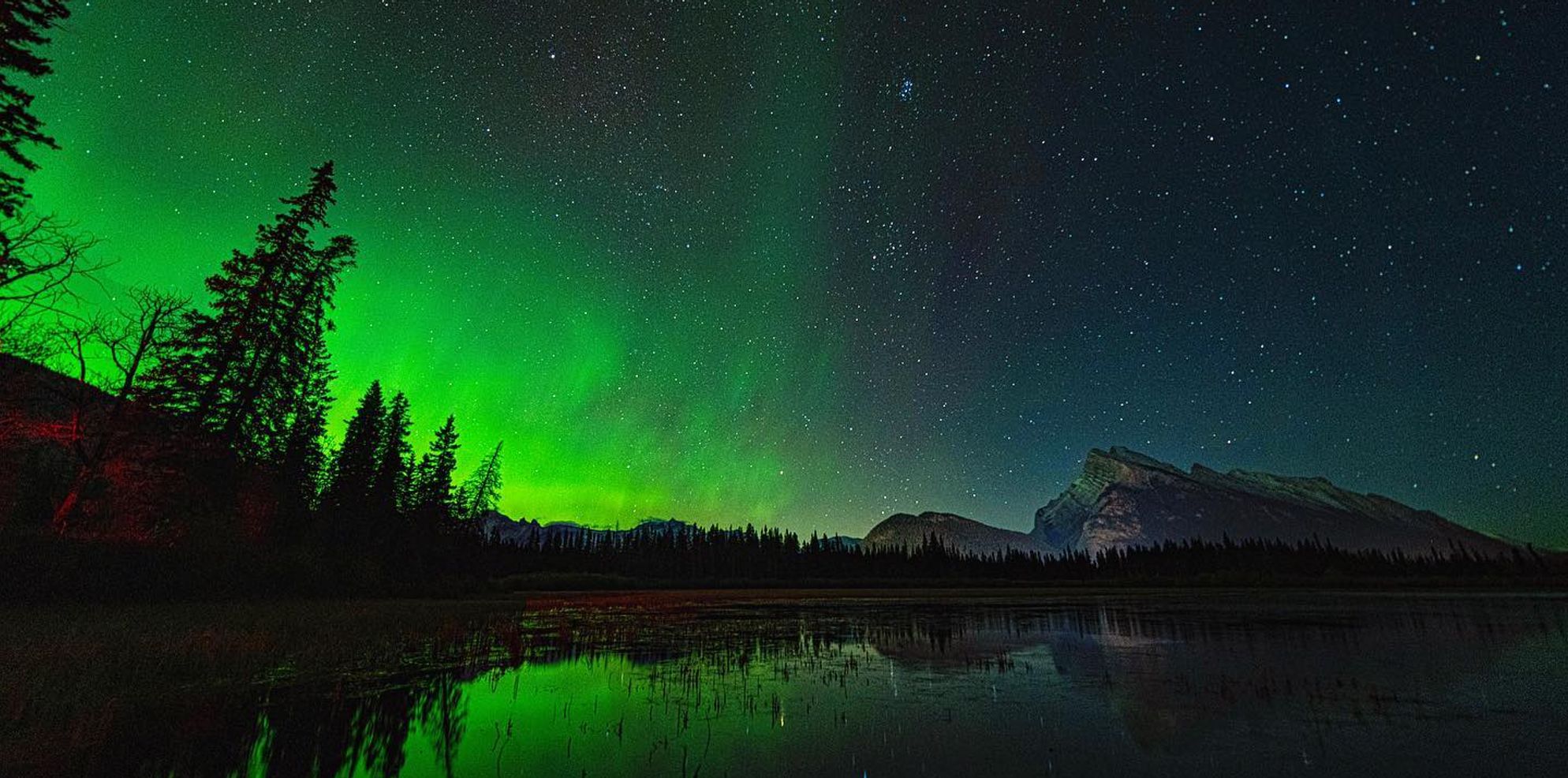 Green aurora glowing over mountains near at Vermilion Lakes in Banff National Park