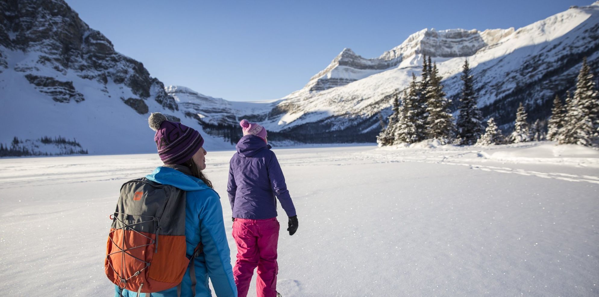 Two people snowshoeing along a frozen lake on a sunny winter day
