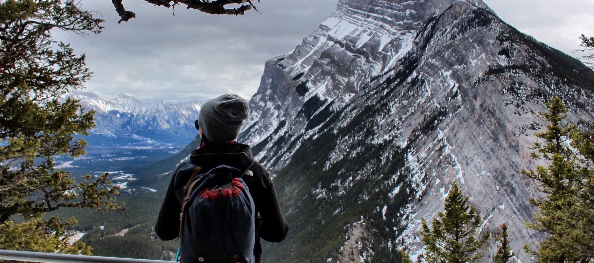 A woman stands on Tunnel Mountain looking towards Mountain Rundle surrounded by trees in Banff National Park.
