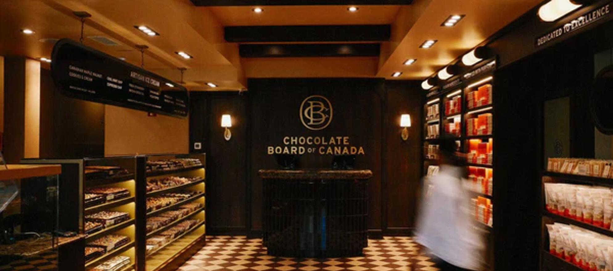 The Chocolate Board of Canada brick and mortar store interior. Brown and white tile floors, dark brown shelves and display cases, and golden yellow ceiling paints