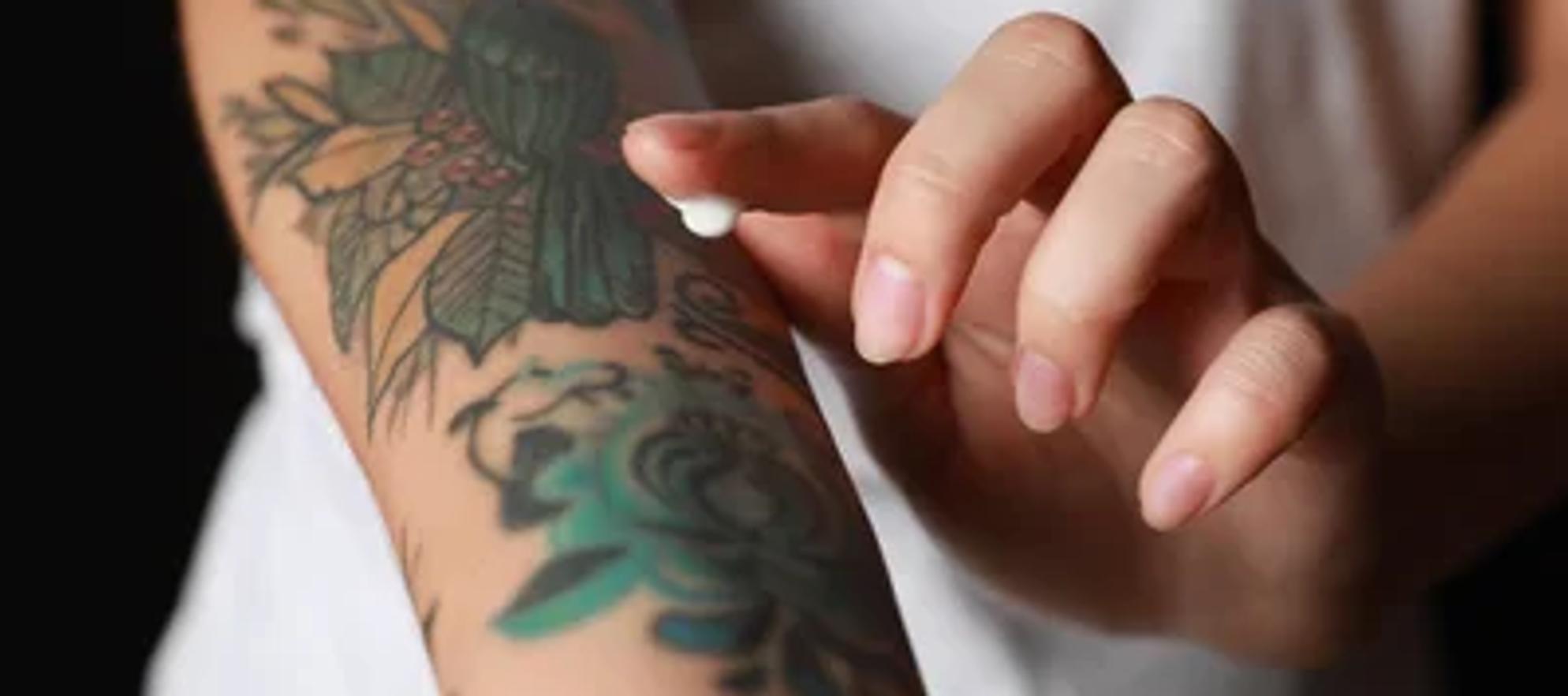 a person putting aftercare cream on a fresh tattoo on their forearm
