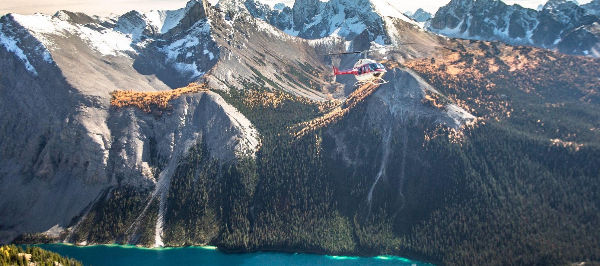 Helicopter flying over a blue lake and orange larch trees