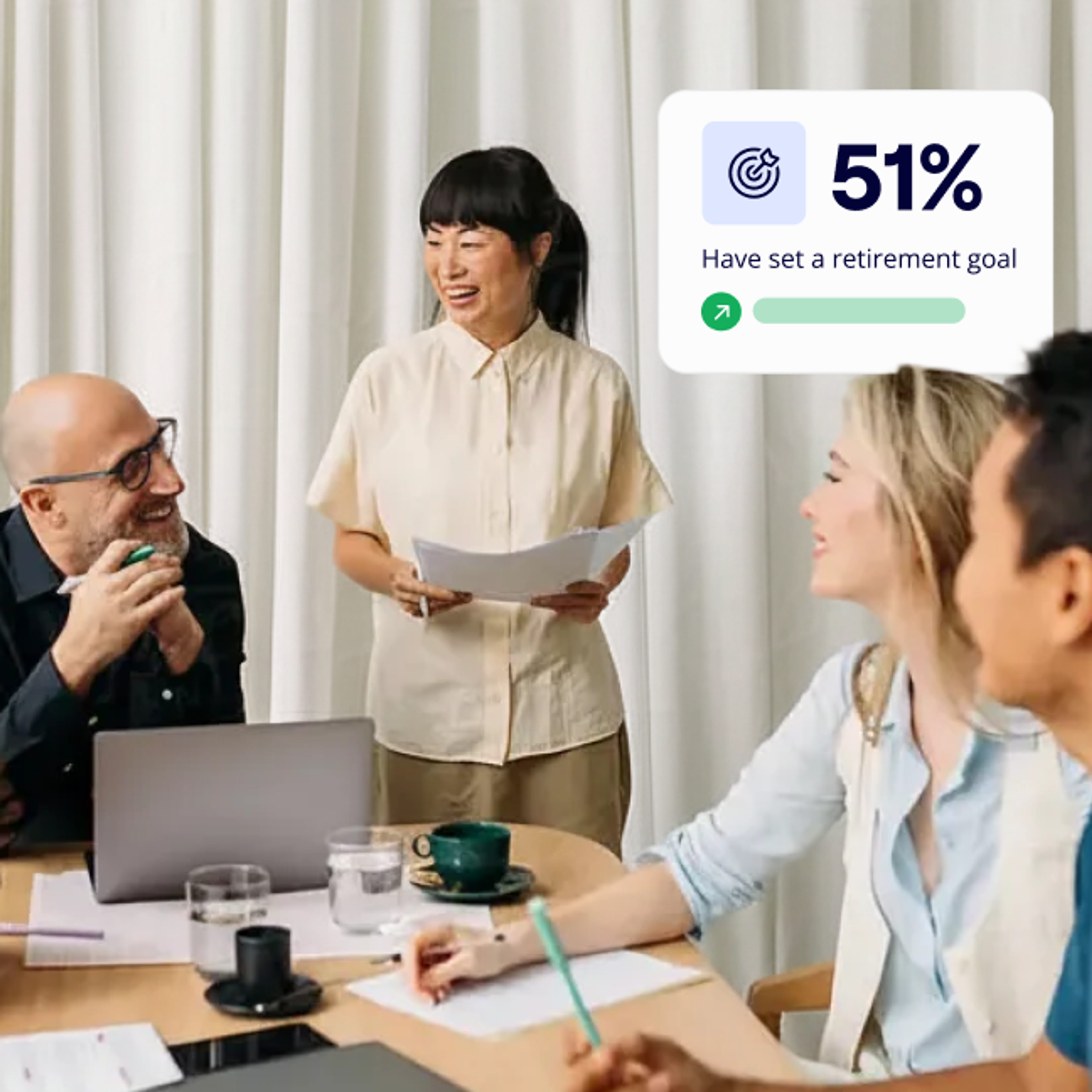 A group of four colleagues sit around a table engaged in discussion, with a standing woman holding papers and a graphic indicating 51% have set a retirement goal.