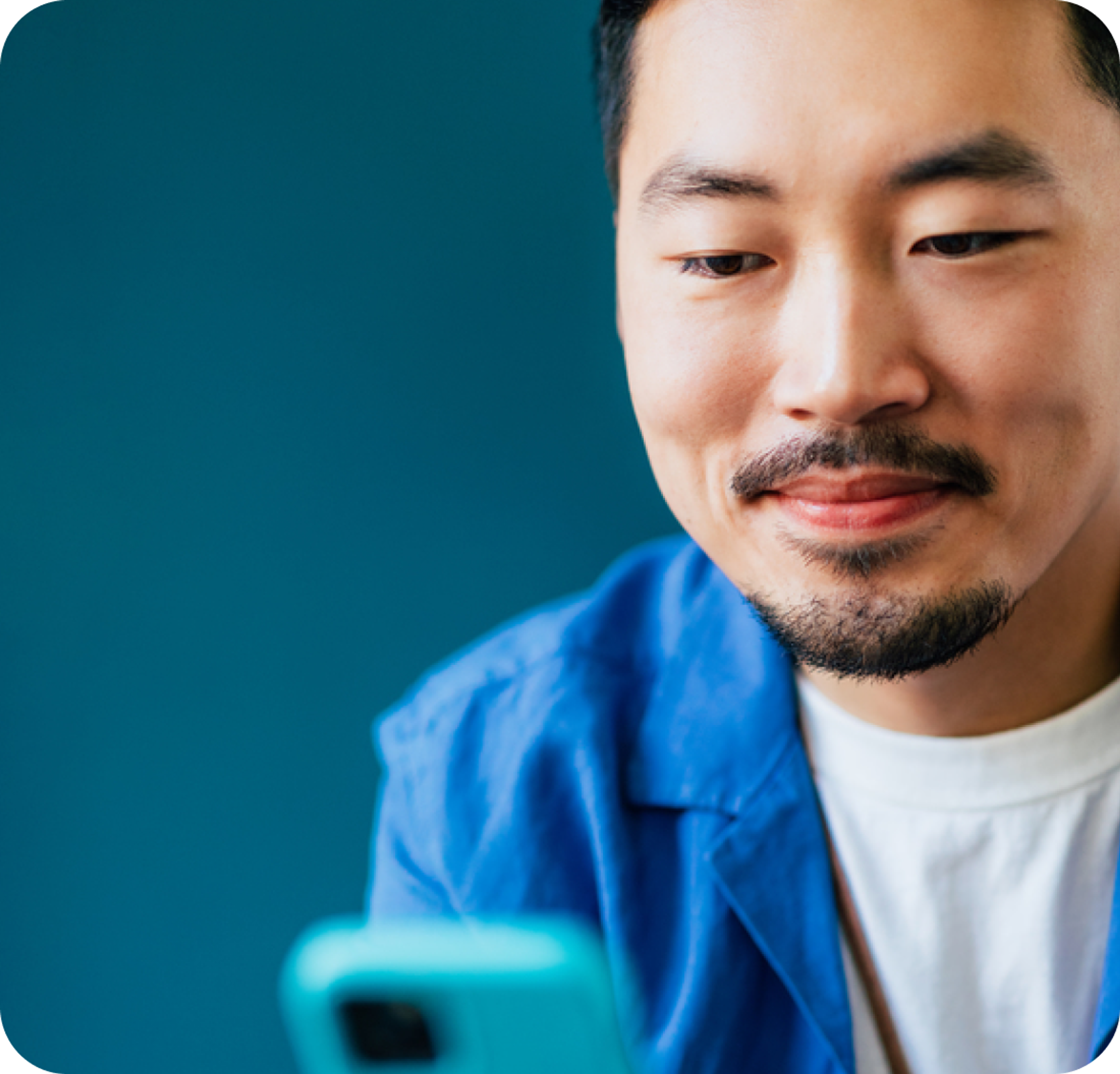 A headshot of a man smiling while looking at a phone