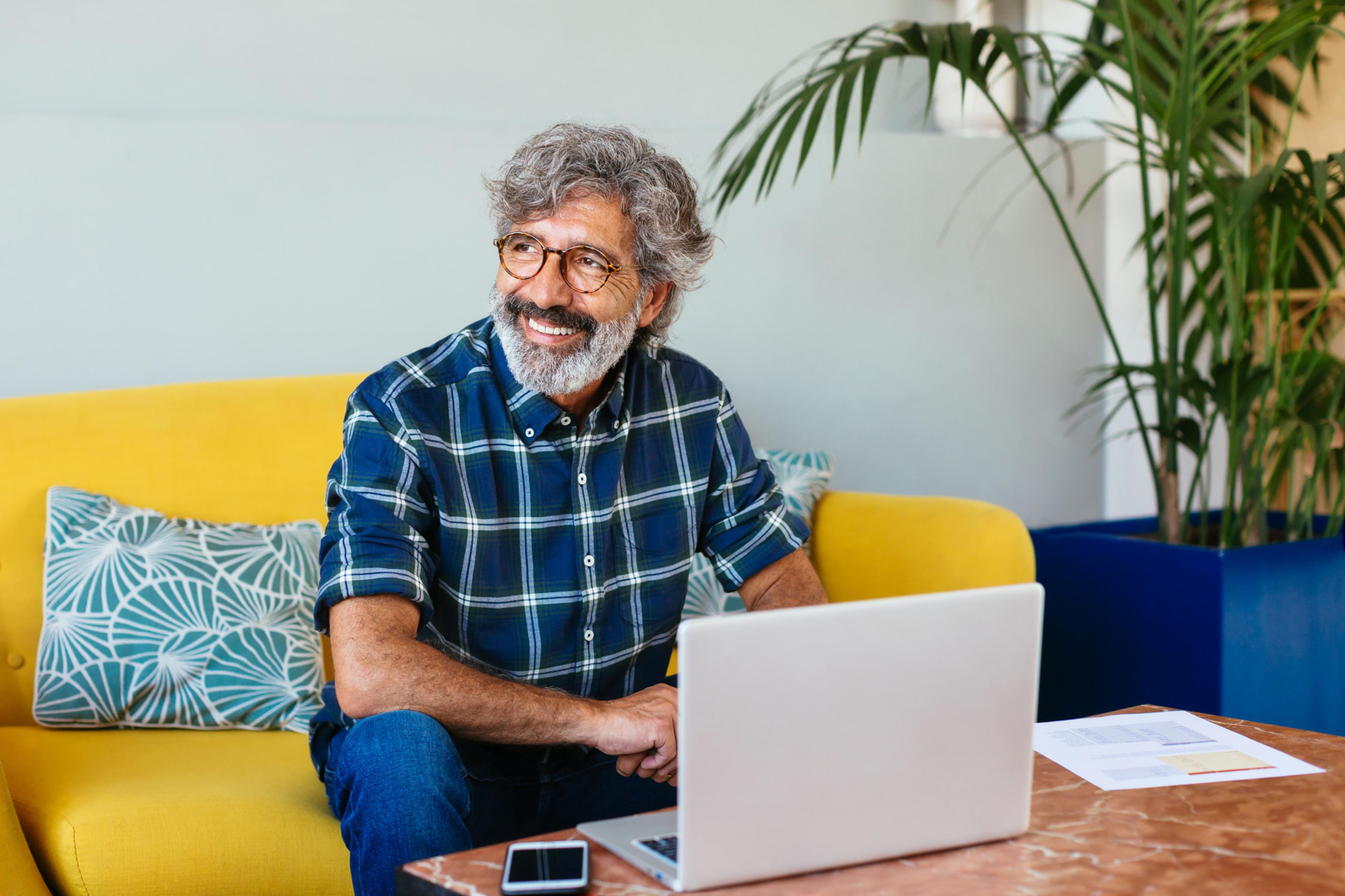 A photo of a man sat down in front of a laptop and smiling