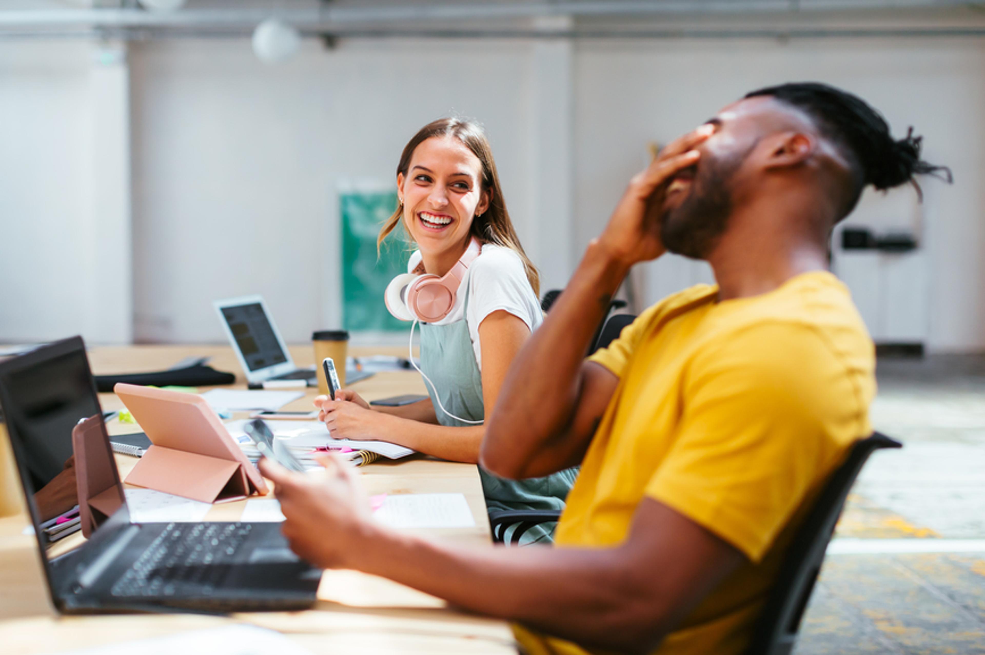 A photo of two colleagues laughing while sat at their desks