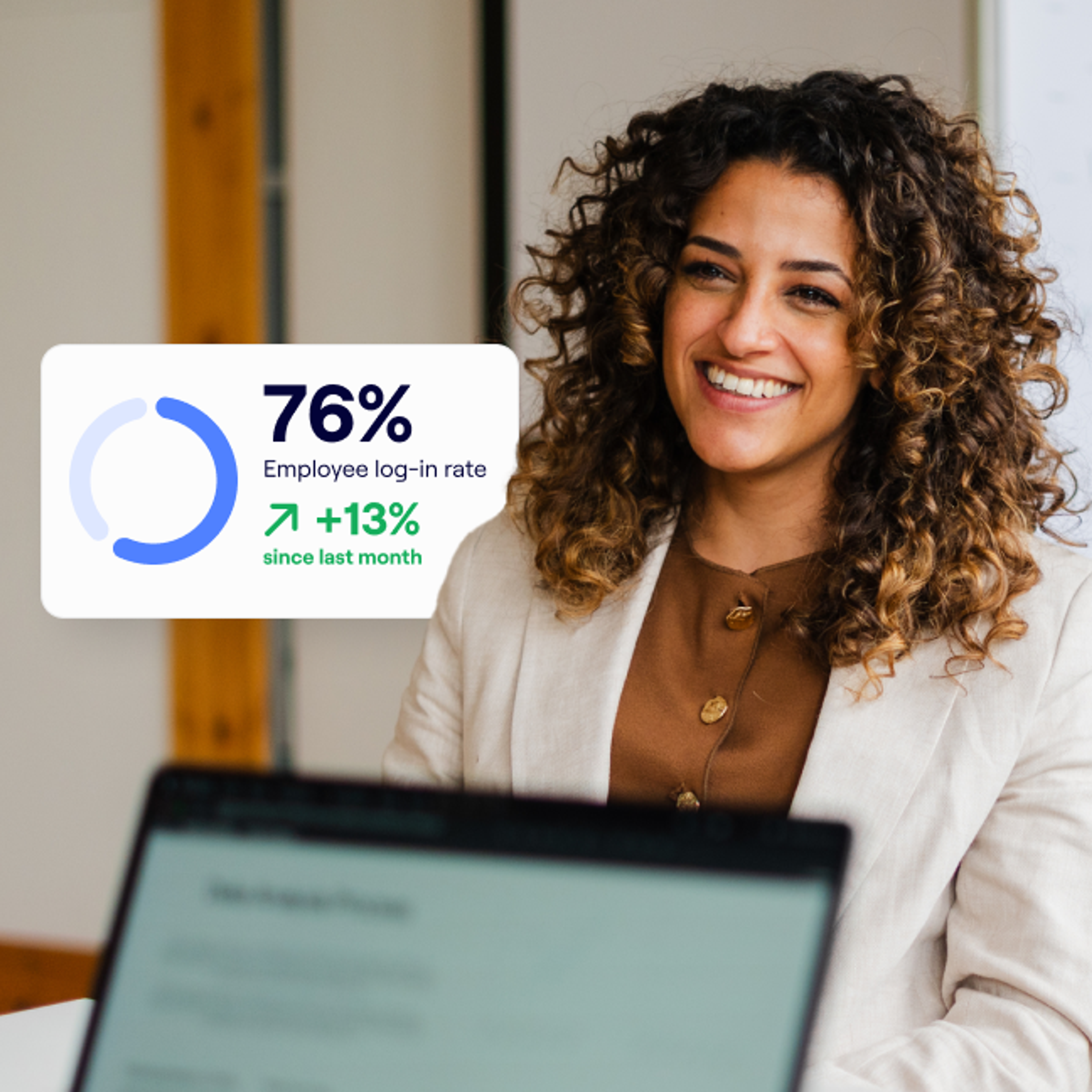 A woman with curly hair and a tan blazer smiles across a desk from someone working on a laptop, while a graphic shows a 76% employee log-in rate with a 13% increase since last month.