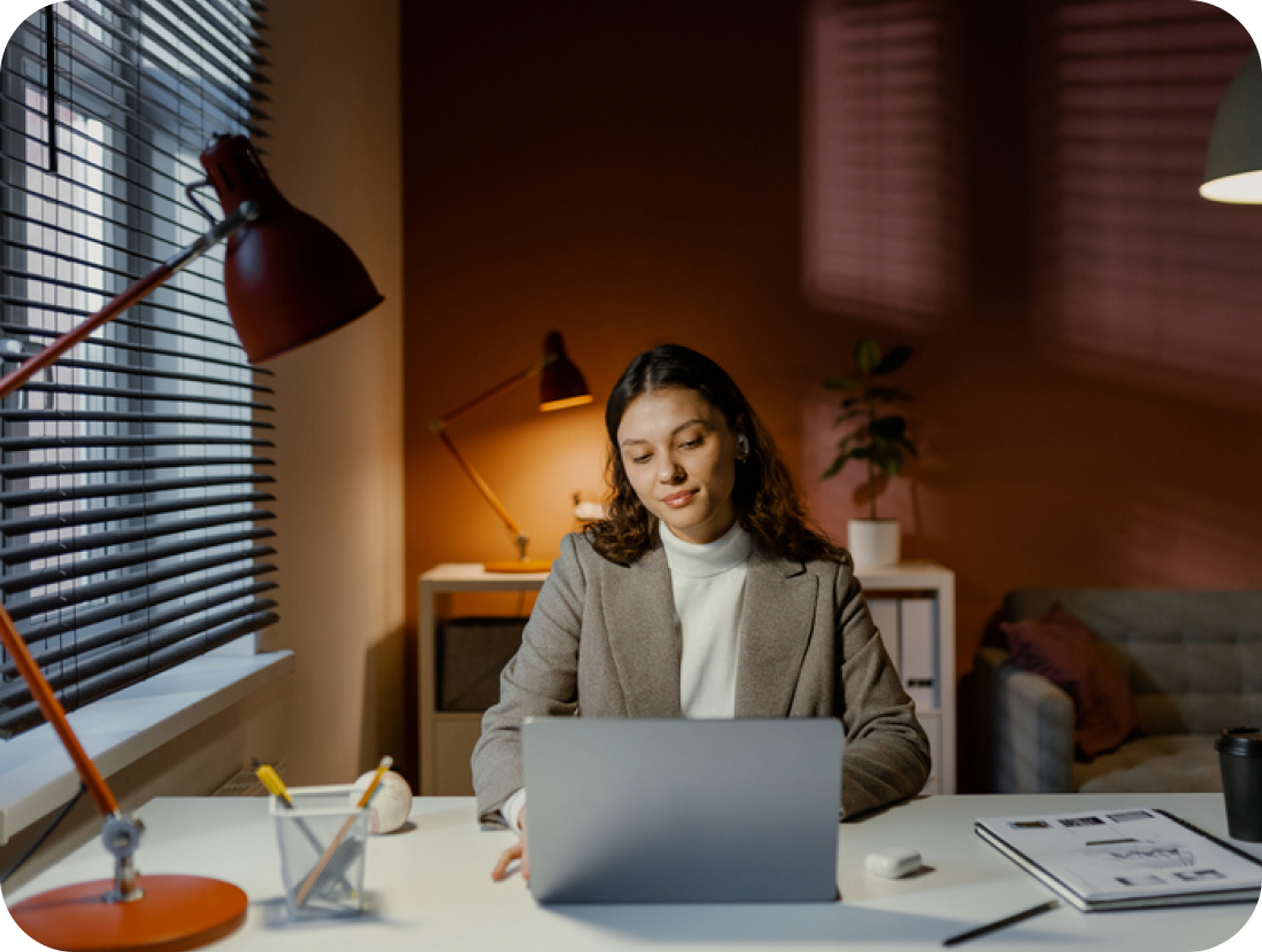 A photo of a woman sat at a desk looking at a laptop