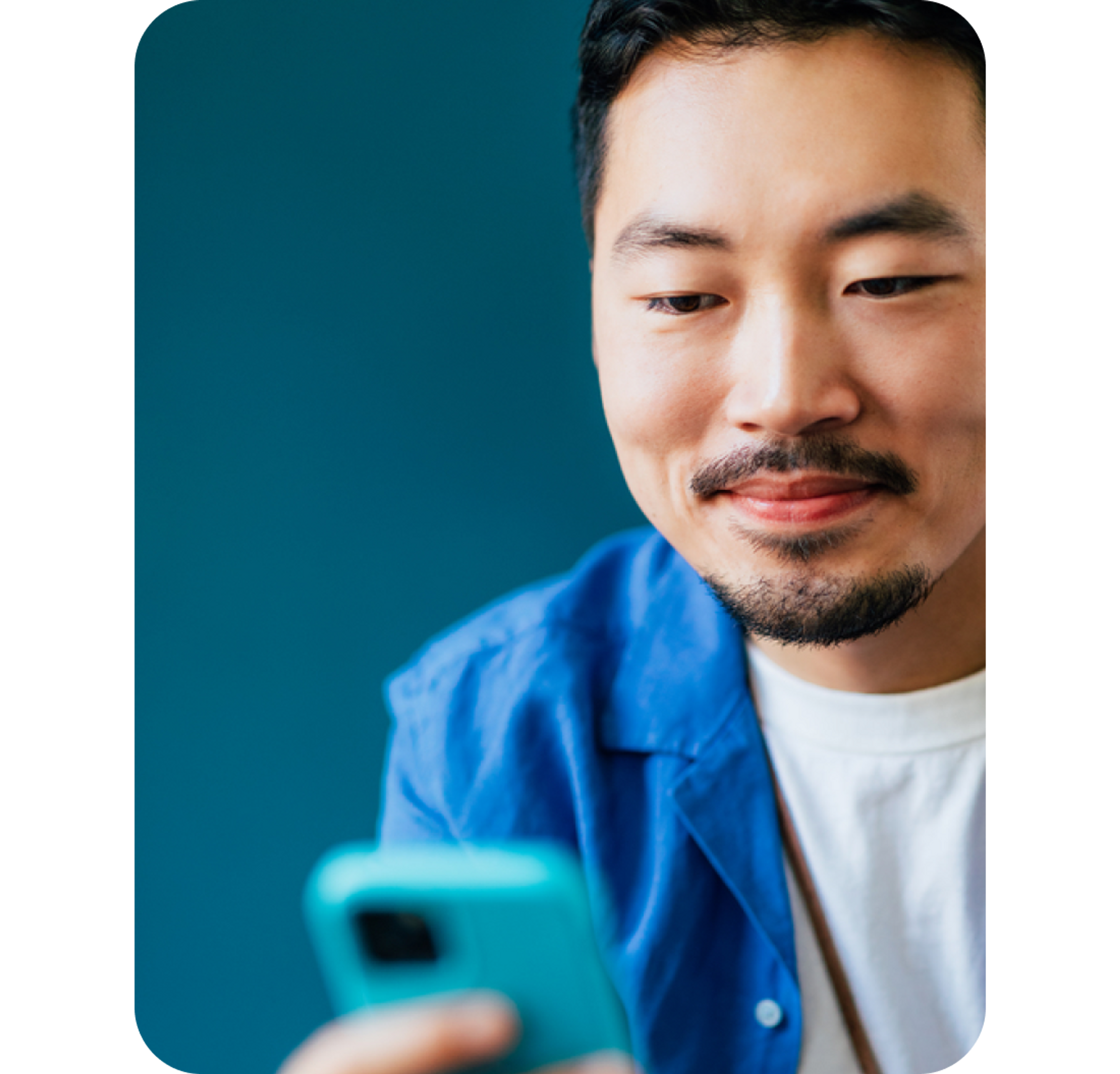 A close up headshot of a man smiling while looking at a phone
