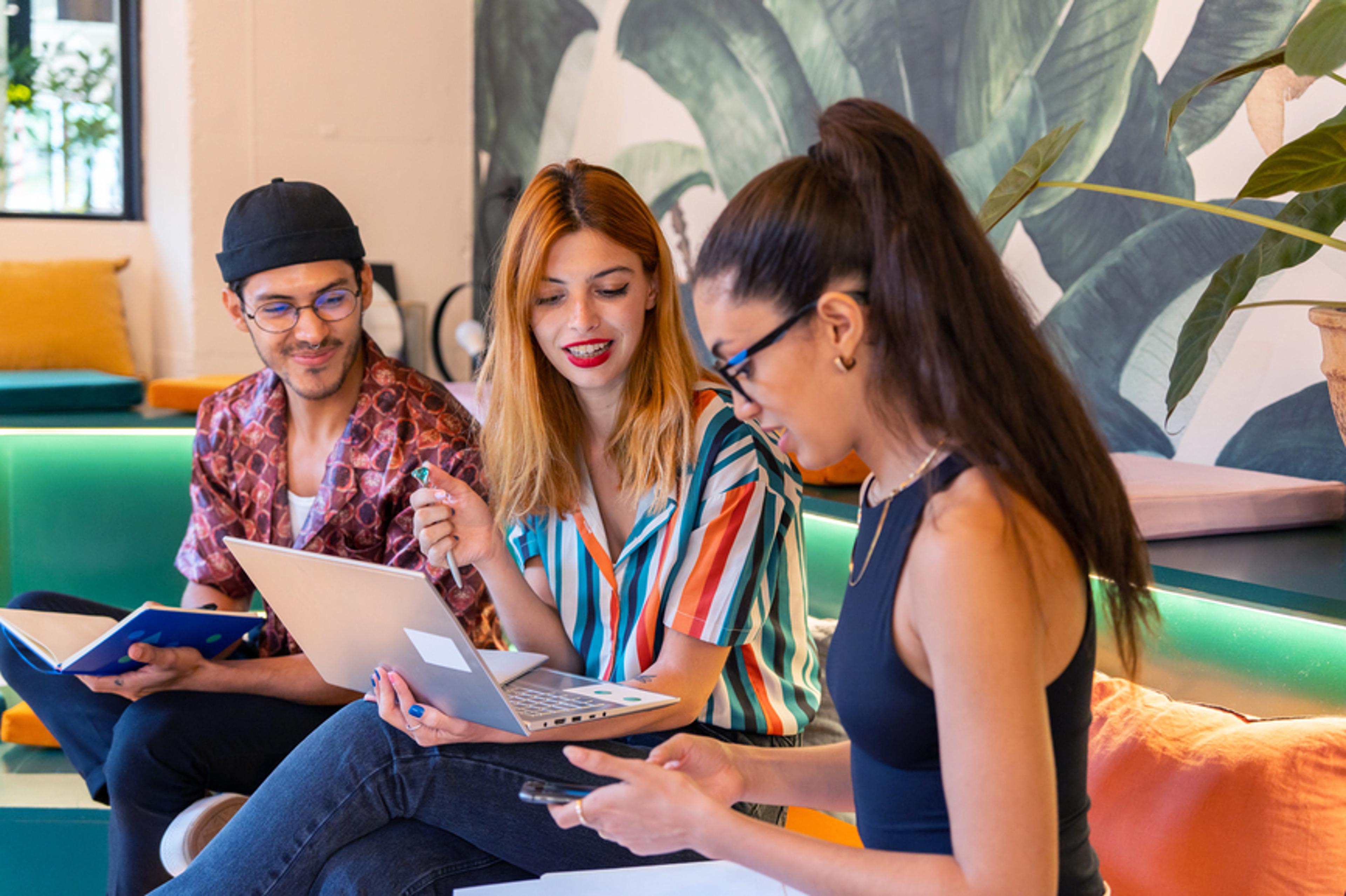 A photo of a team of three people sat down and looking at a laptop screen