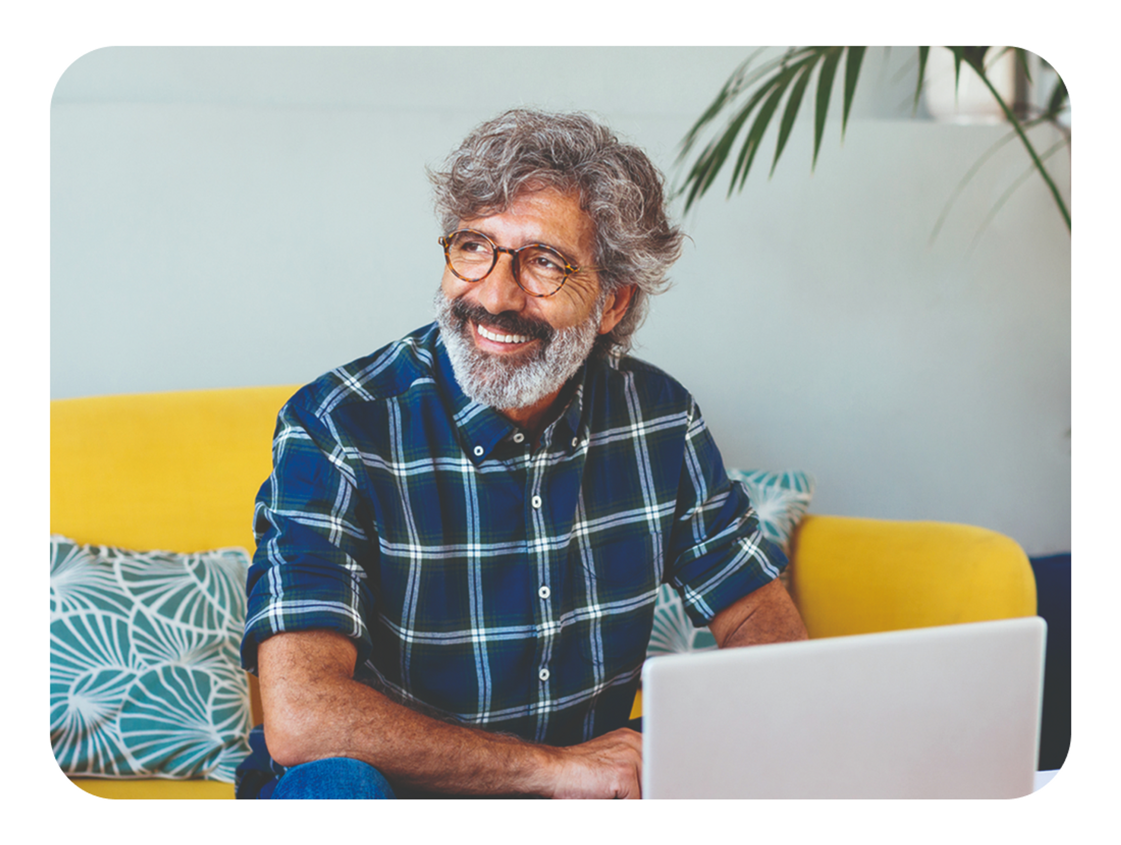 A photo of a man sat down and smiling in front of a laptop