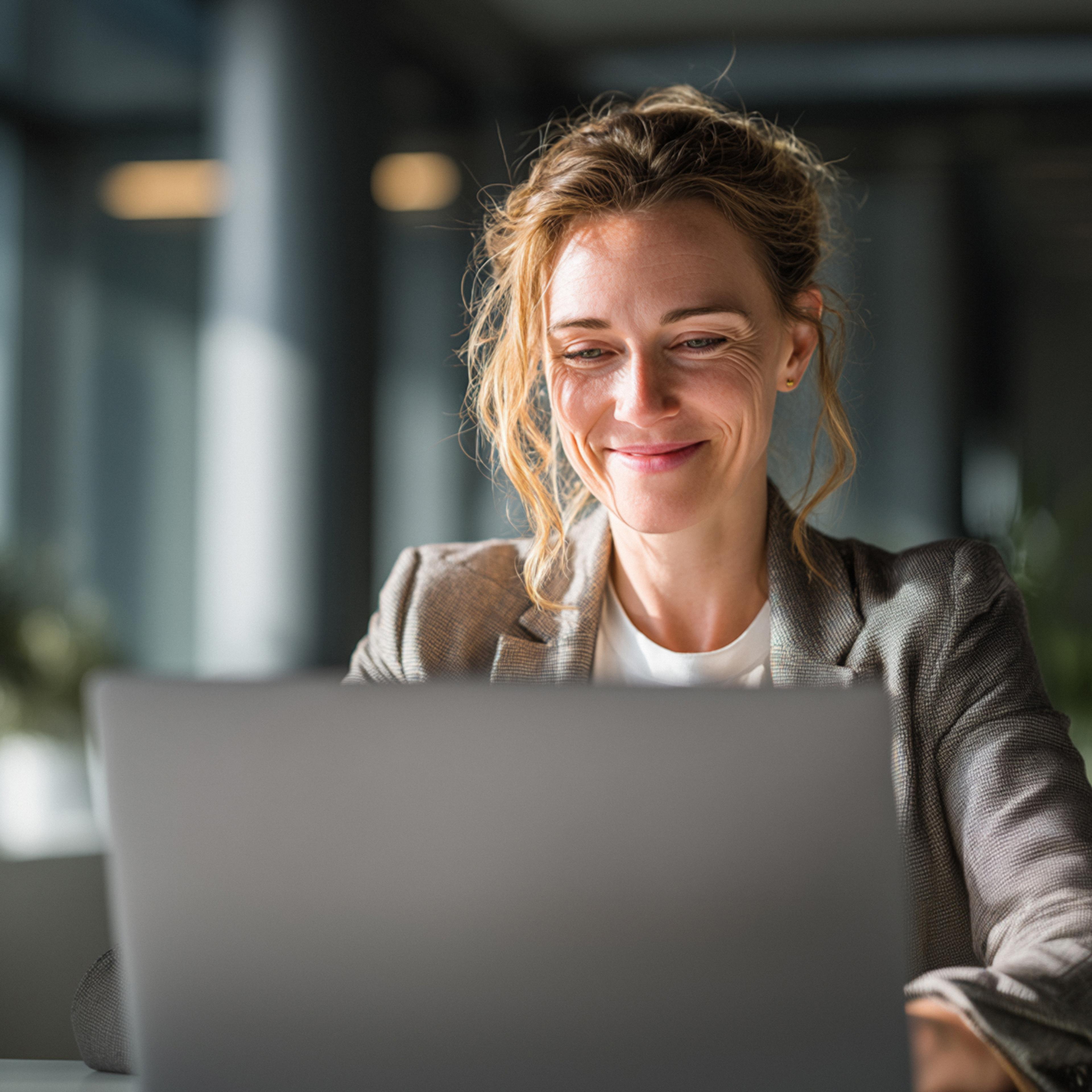 Blonde woman sitting at a desk in an office looking at laptop screen
