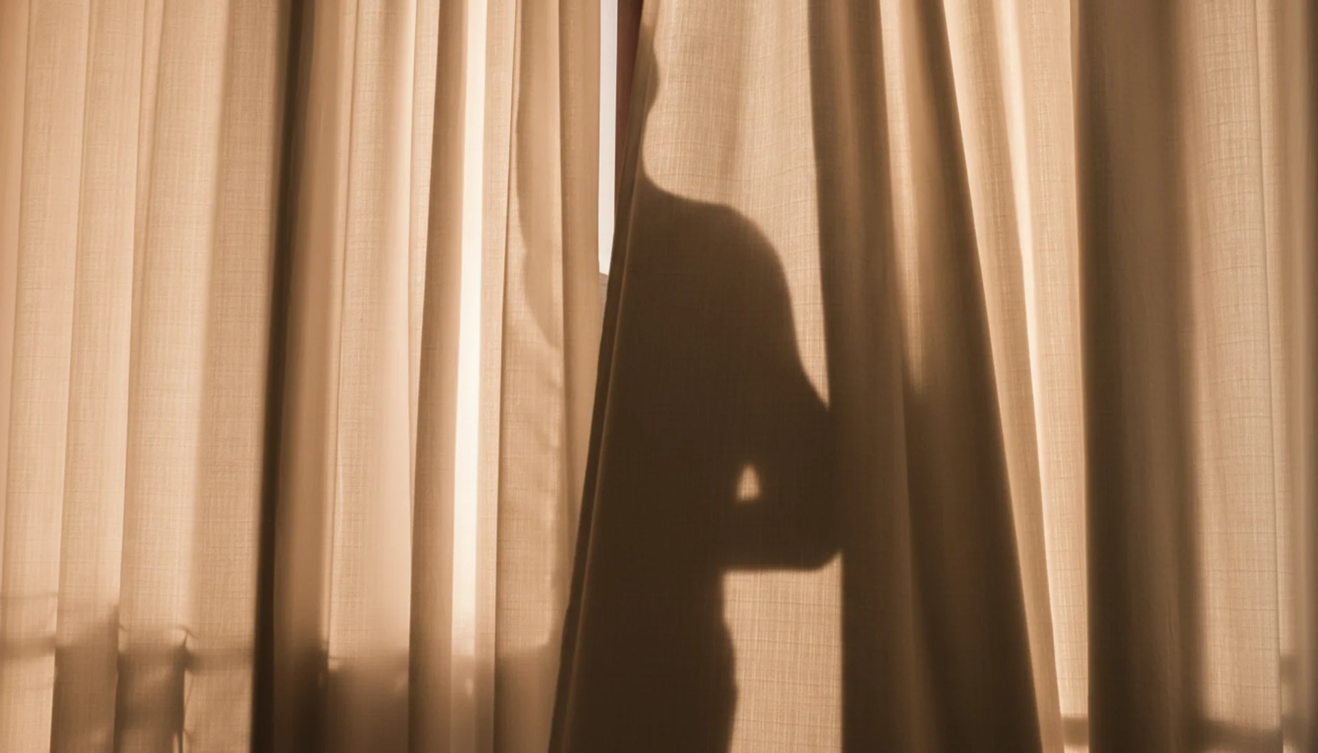 Silhouette of a person behind a curtain, only the upper half of the torso visible.