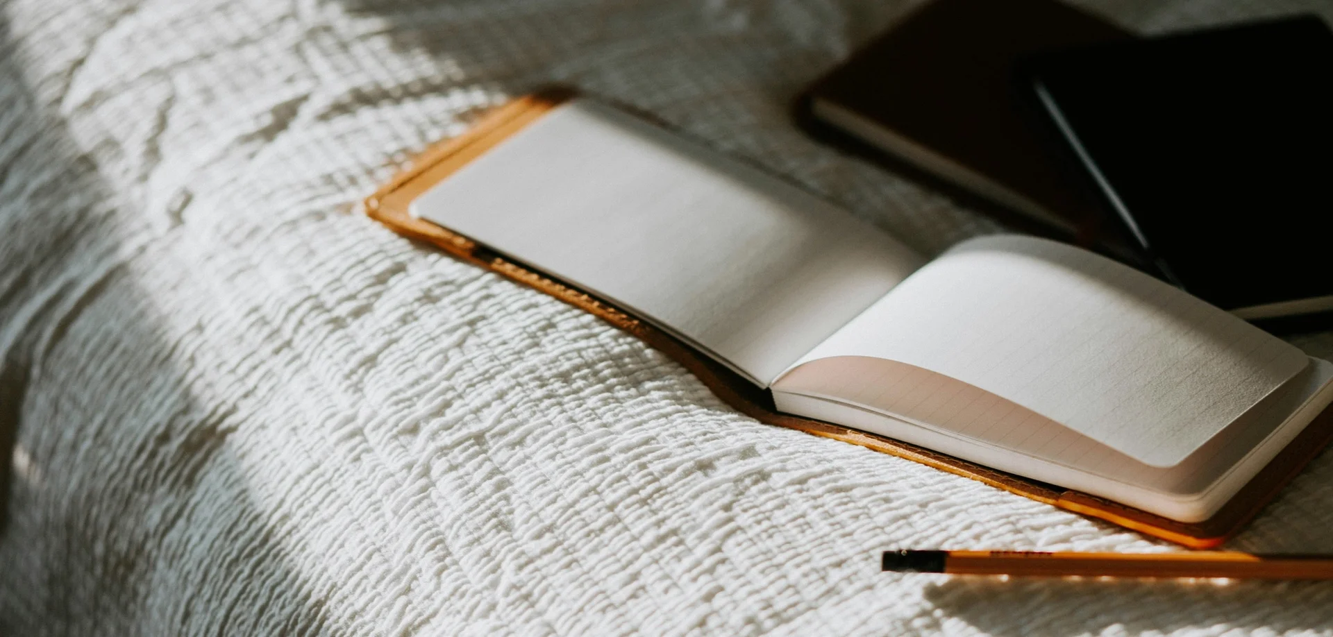 Open notebook on a bed with a pencil beside it