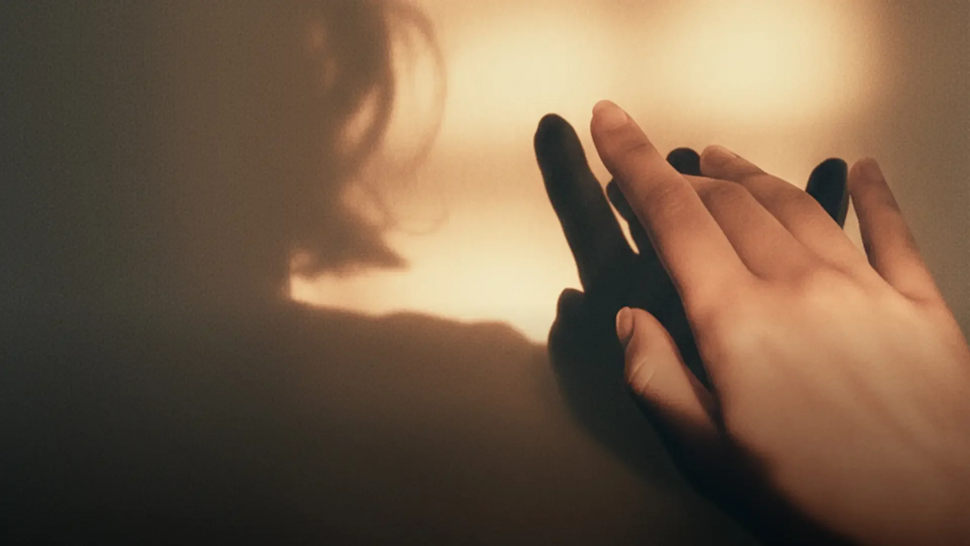 A hand reaches into warm light, casting a long shadow on a soft background.
