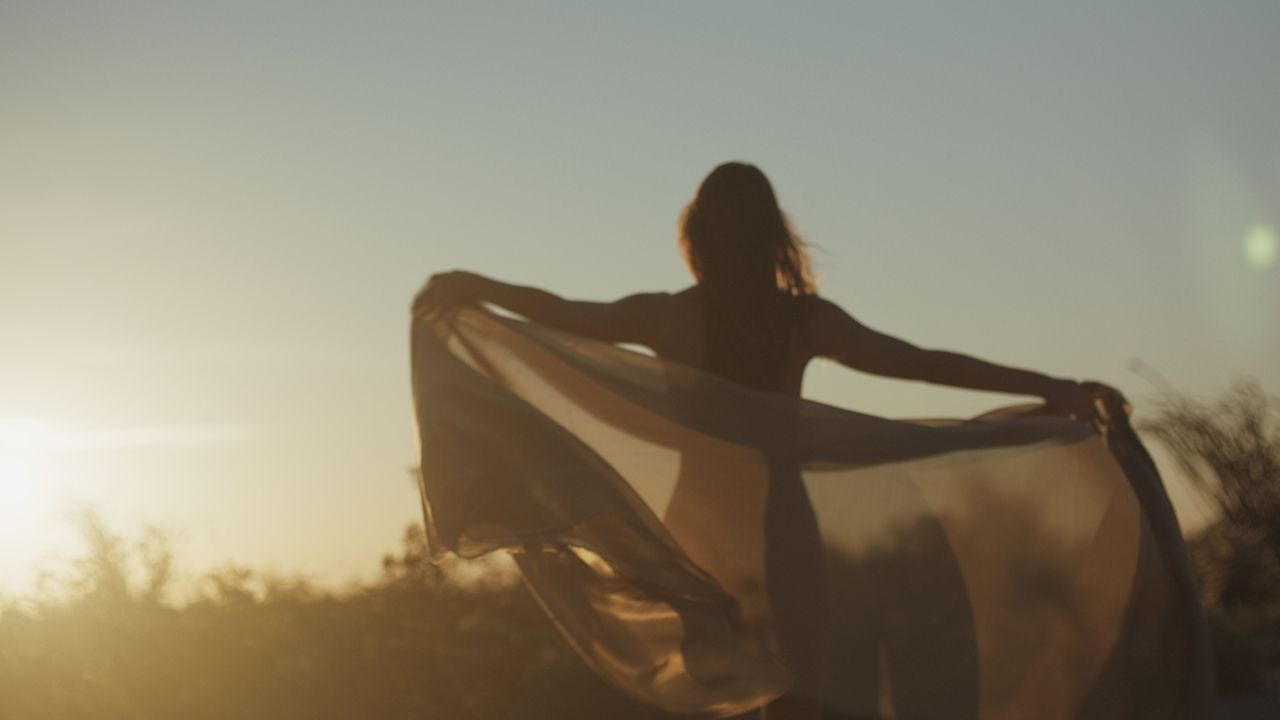 Woman dancing in a field, holding a silk scarf flowing in the wind