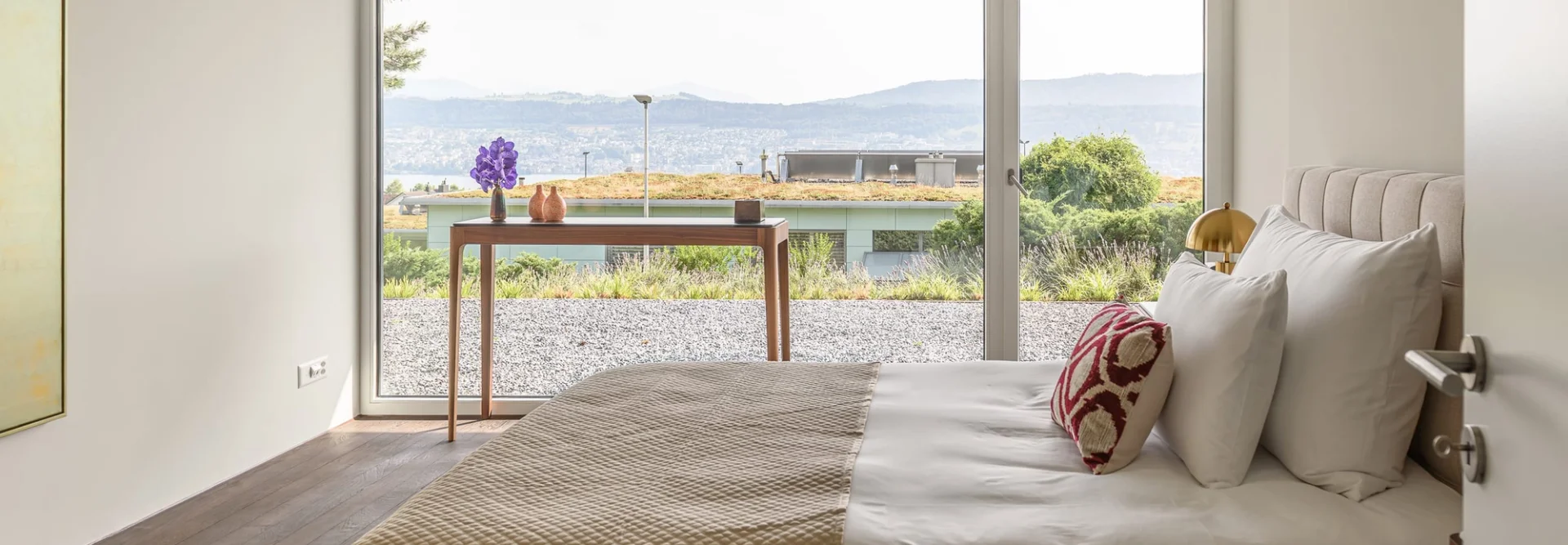 Bright bedroom with a neatly made bed and mountain view through floor-to-ceiling windows