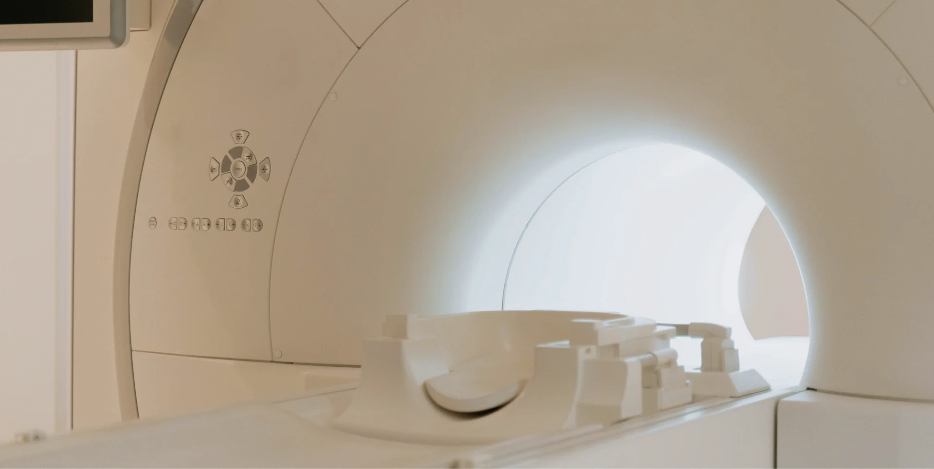 The clean, light-colored interior of an MRI machine, showing the bright tunnel opening and the patient examination bed or table extended forward.