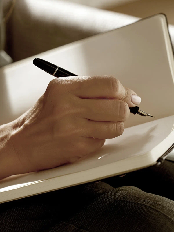 Hand holding a fountain pen over an open notebook.