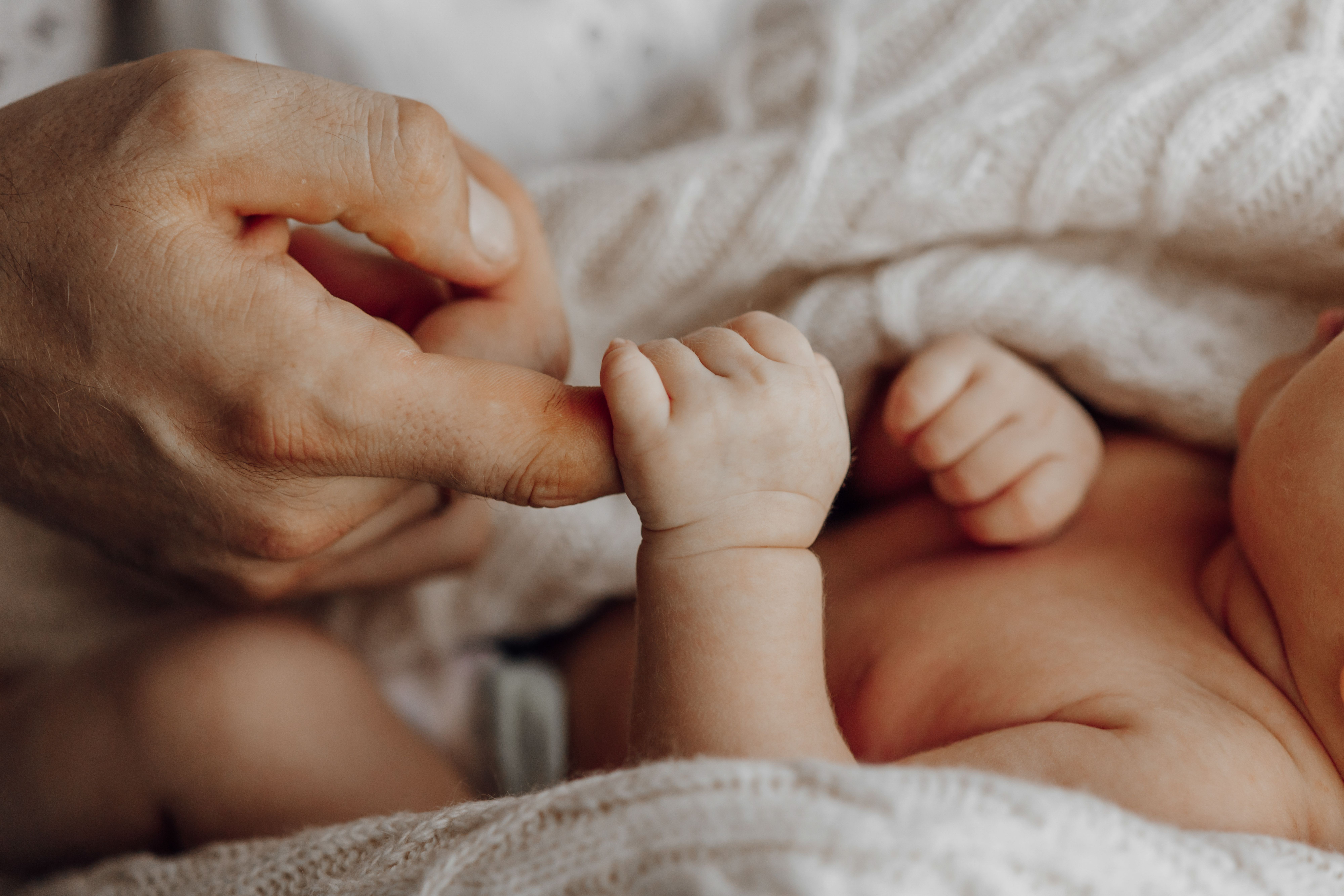 One baby’s hand is holding another’s