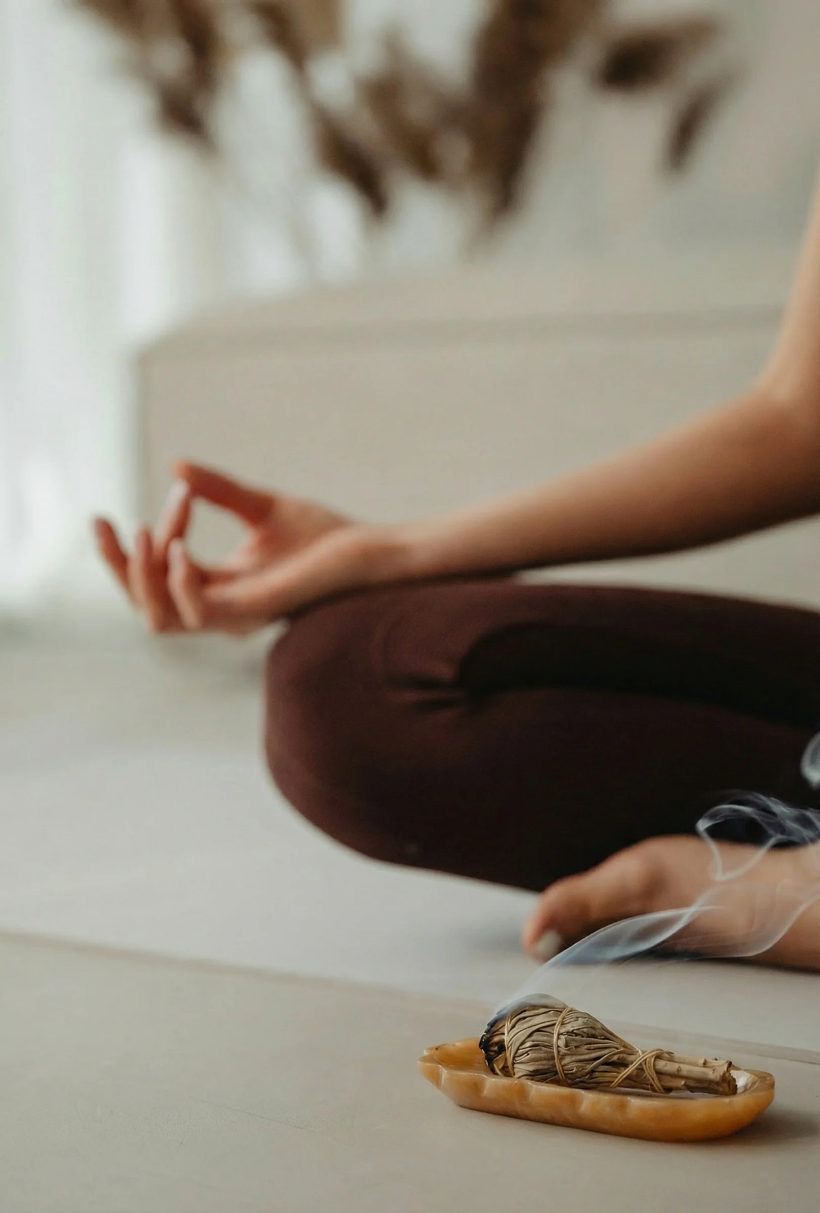 Woman sitting cross-legged, only part of knee, arm, and foot visible, with a sage bundle for smudging in front of her