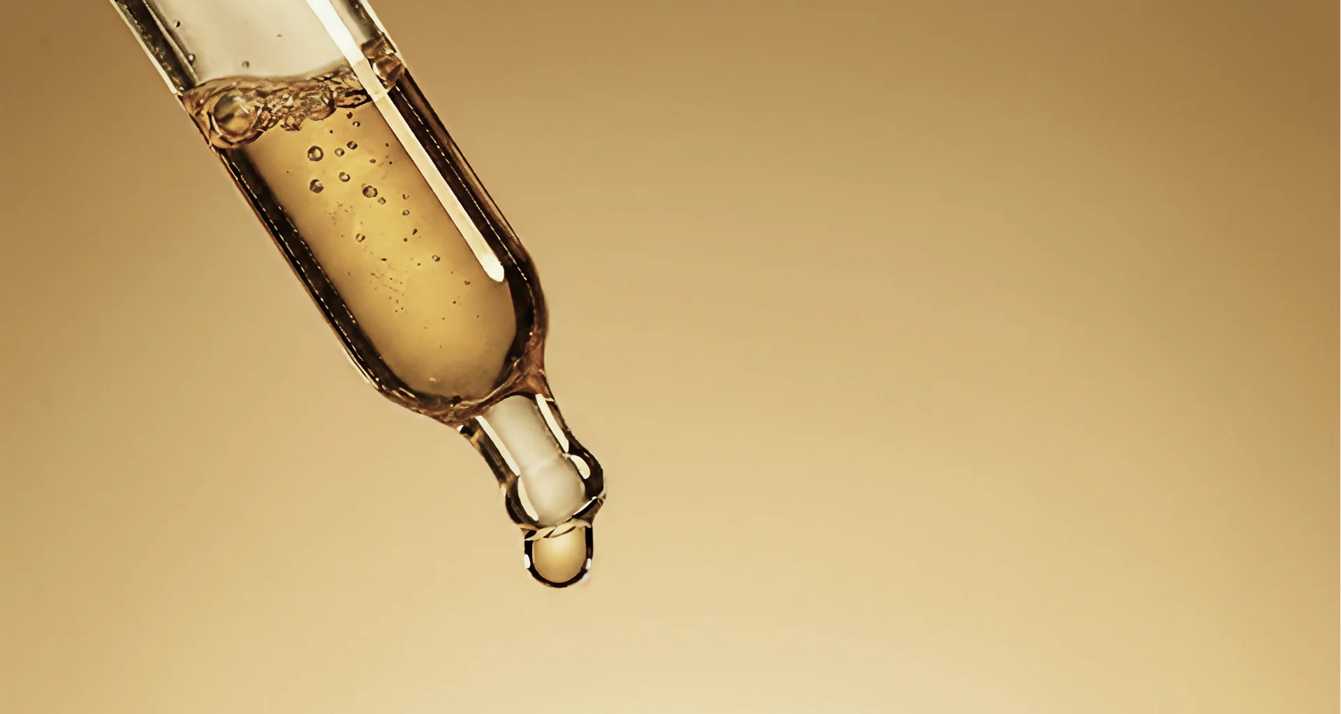 Golden liquid in a dropper with a single drop about to fall.