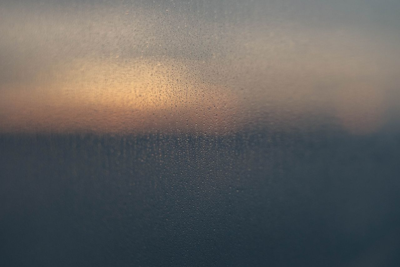 Window with raindrops, dark mood outside at sunset, blurred view