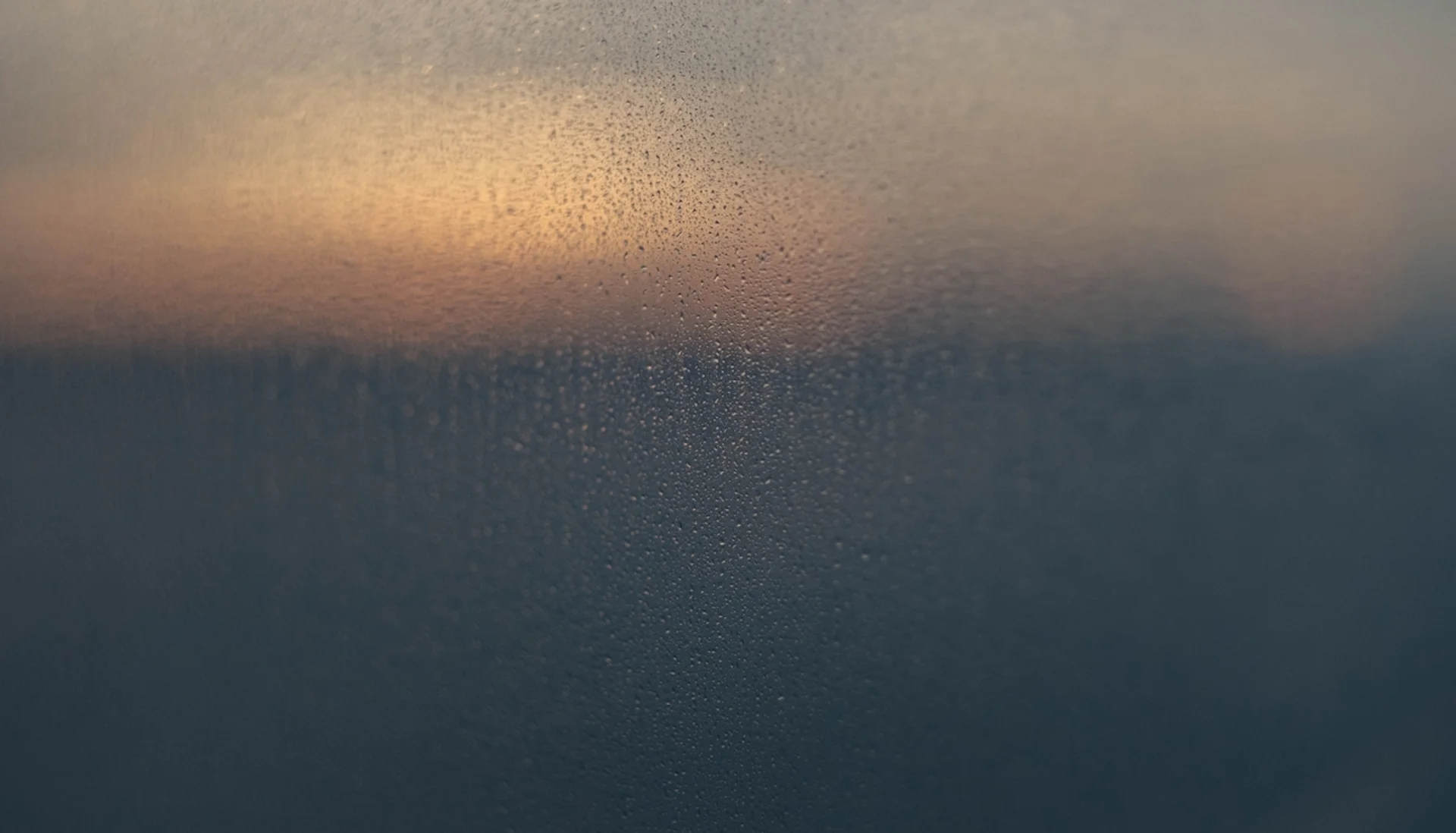 Window with raindrops, dark mood outside at sunset, blurred view