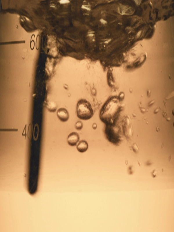 A close-up shot inside a graduated beaker shows a warm-toned liquid vigorously boiling with numerous bubbles, alongside visible measurement markings for 600 and 400.