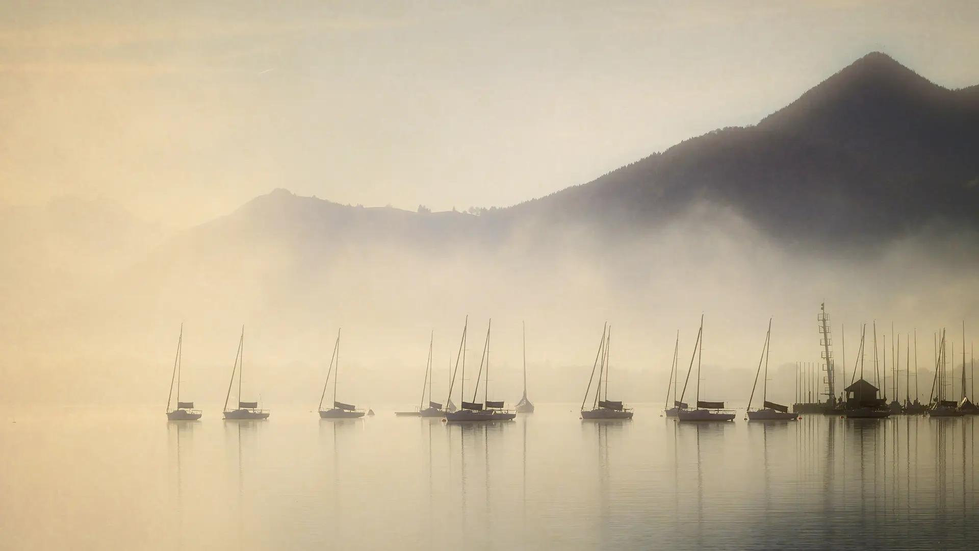 View of a lake with floating boats in the misty morning light