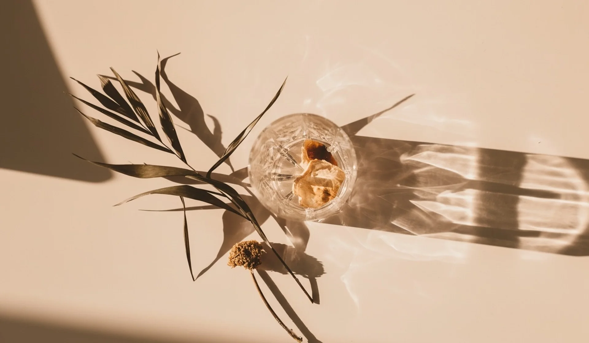 Empty glass containing dried rose petals, with a dried palm leaf beside it