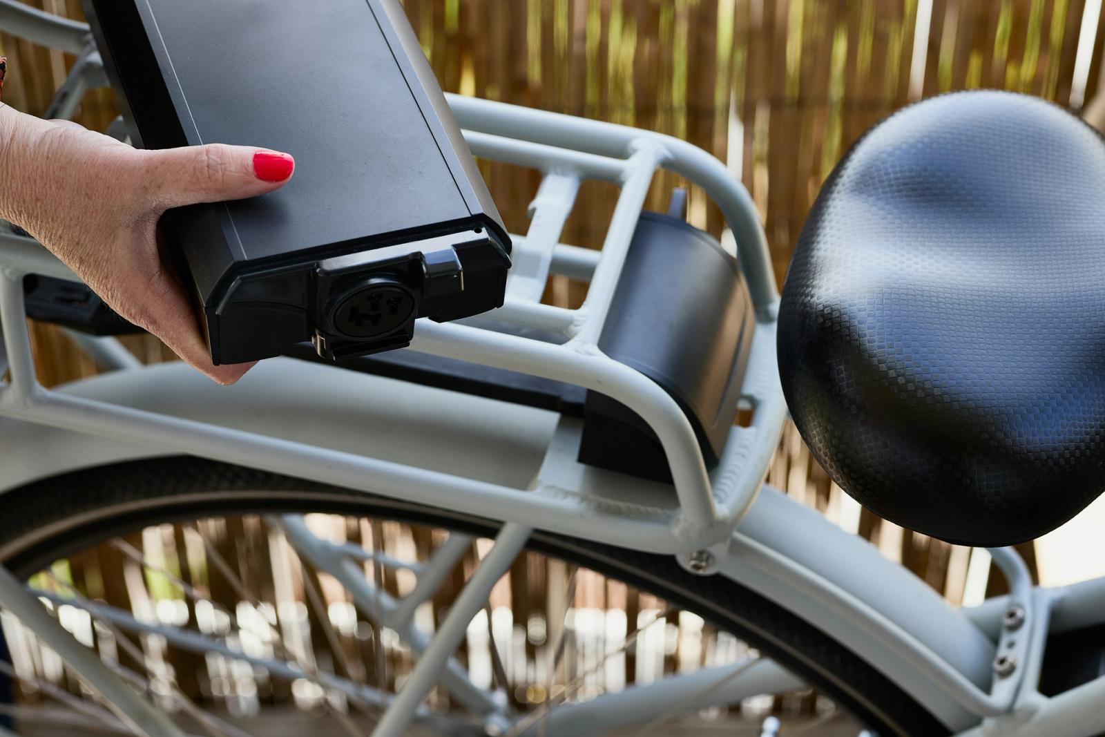 Close-up of a hand sliding a battery out of an e-bike's rear rack