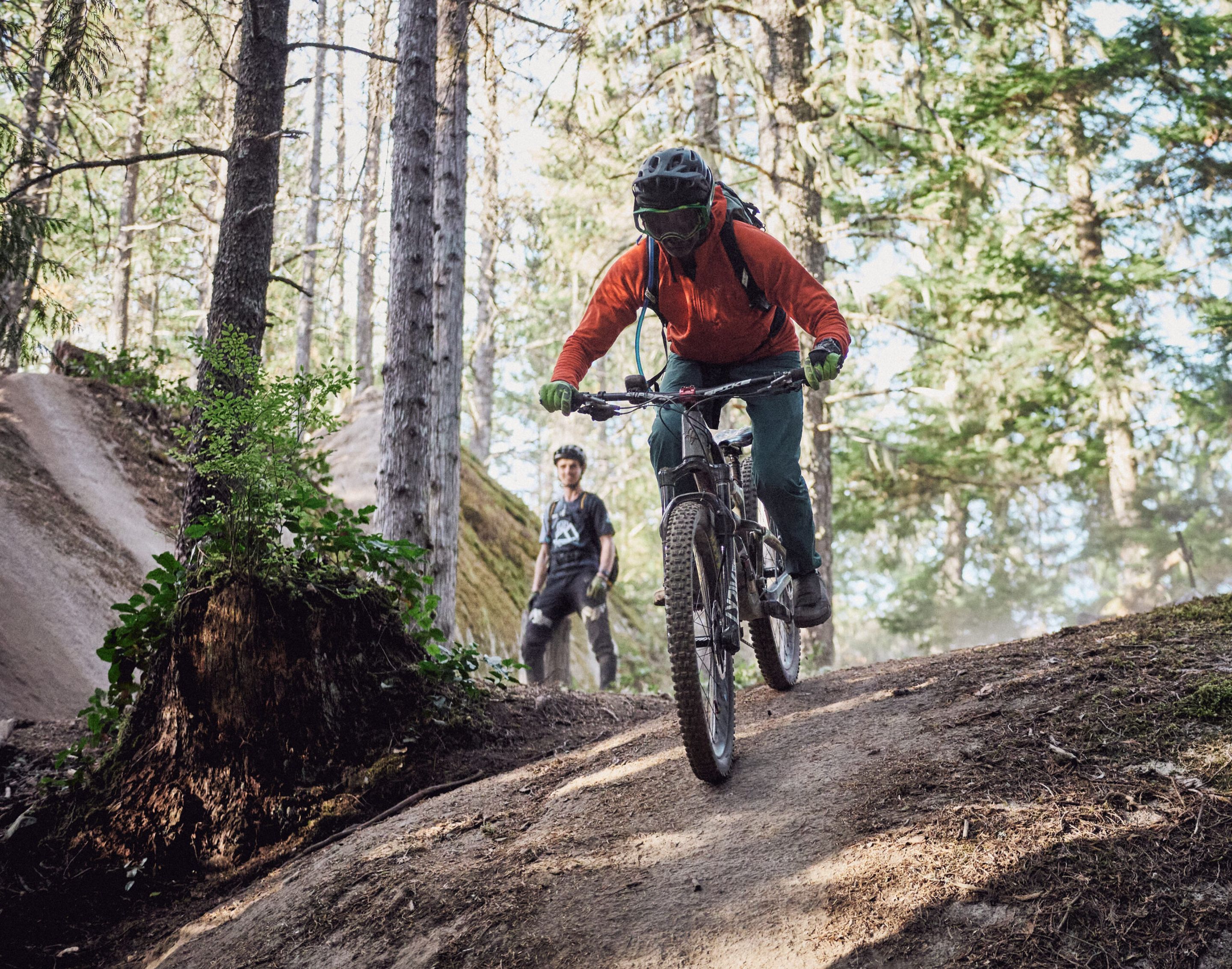 Bike coach in outdoor trail setting showing proper riding posture and technique to a participant during an instructional session.