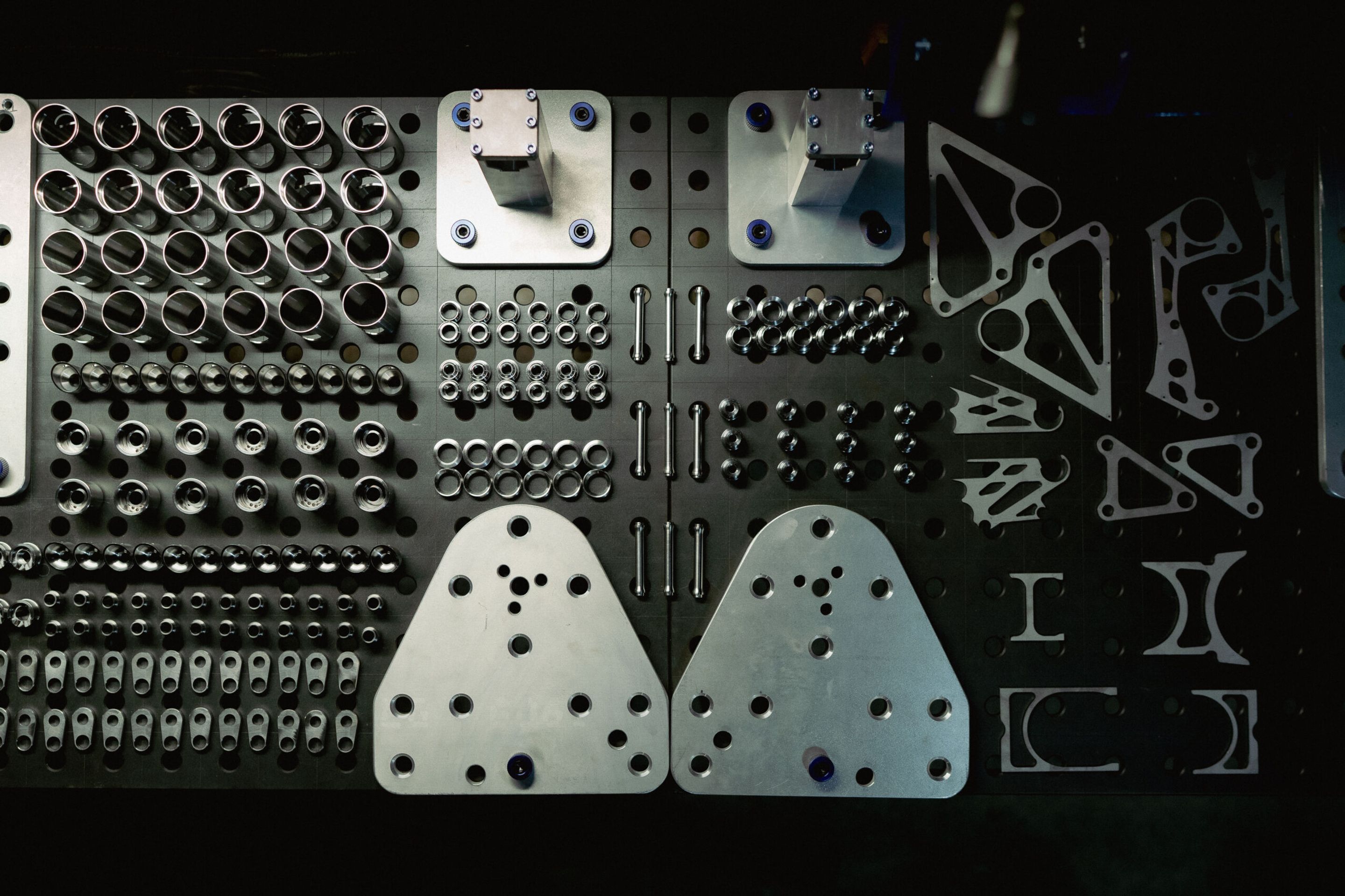 Organized workshop inventory board displaying precision bike components including bearings, spacers, bolts, aluminum fixtures, derailleur hangers, and frame-building jigs at a custom bike manufacturer.