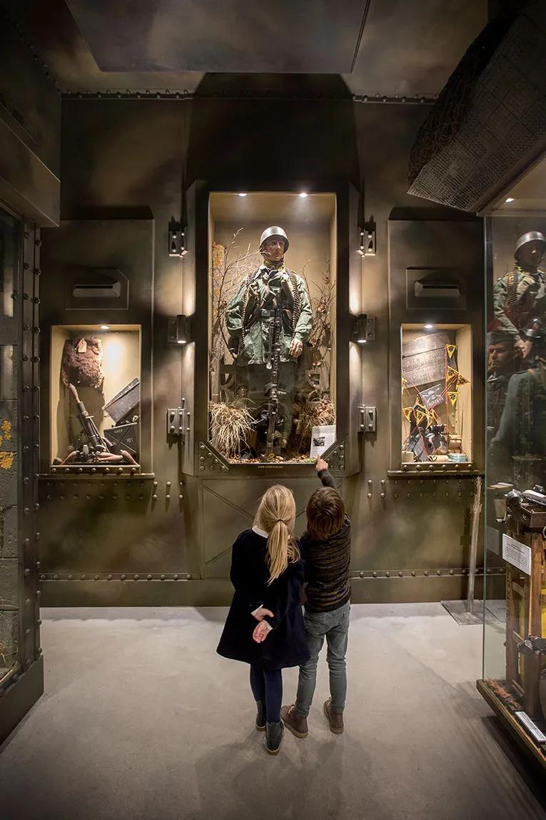 Children look and point at a display case with a mannequin as a soldier.