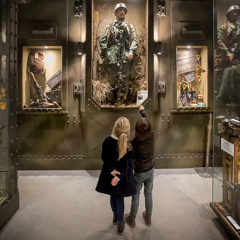 Kindjes kijken en wijzen naar een kijkkast met een mannequin als soldaat.