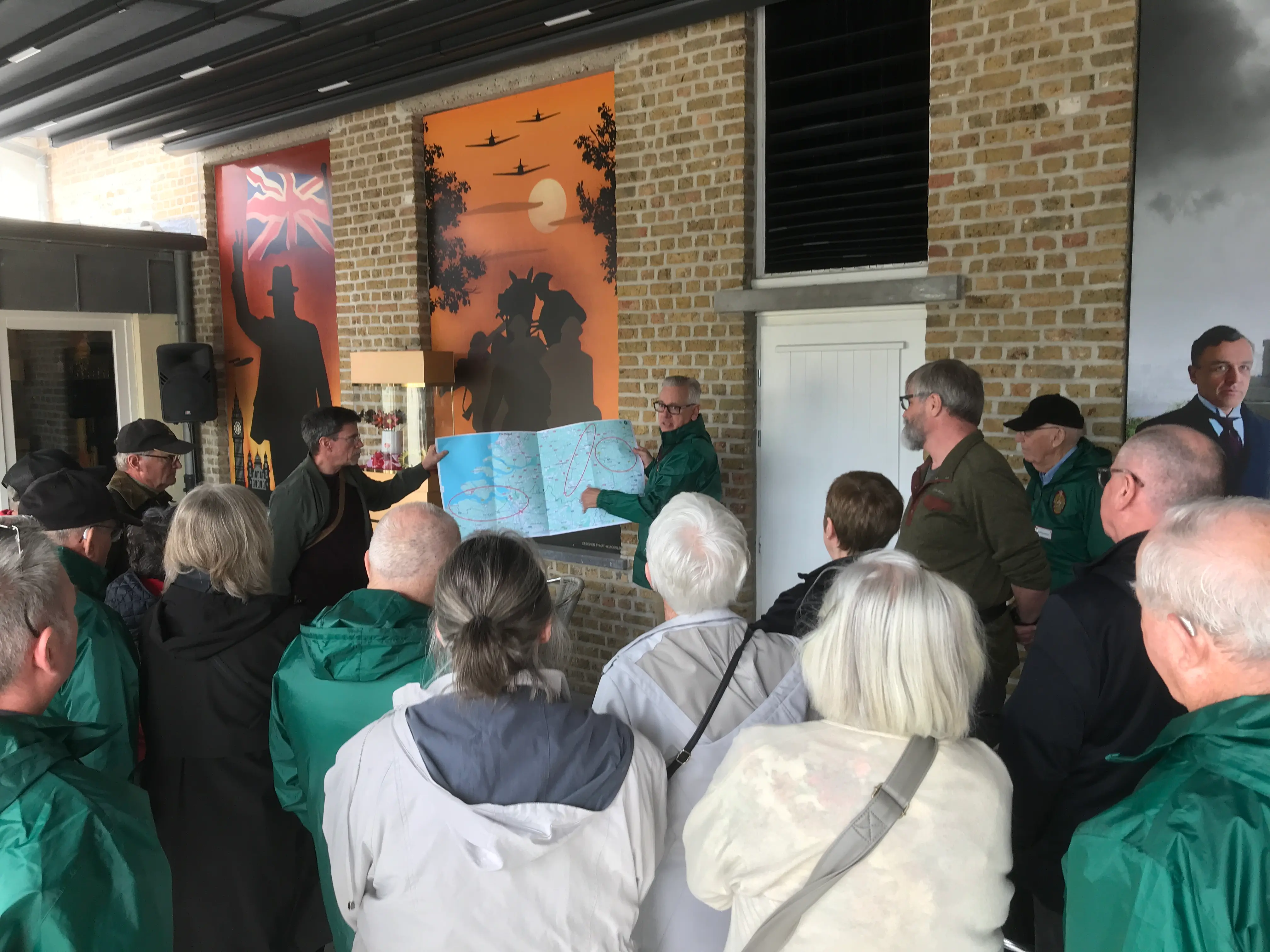 2 gidsen geven uitleg aan de hand van een kaart aan een groep omstaanders
