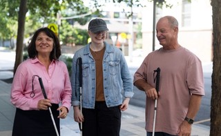Three People standing together with their white canes and smiling.