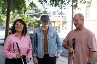 Three Clients standing with their white canes smiling.