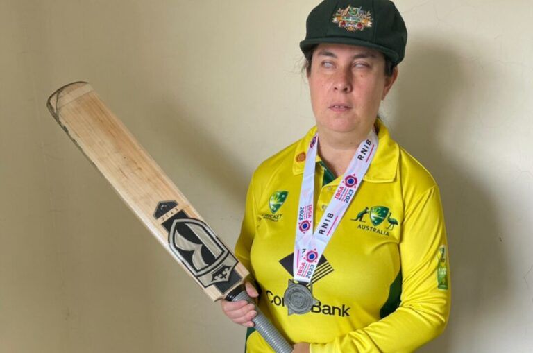 Jennifer standing with a cricket bat in her cricket uniform