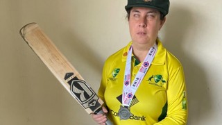 Jennifer standing with a cricket bat in her cricket uniform