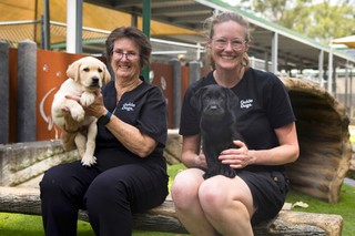 Two Volunteers smiling with yellow Labrador puppies.