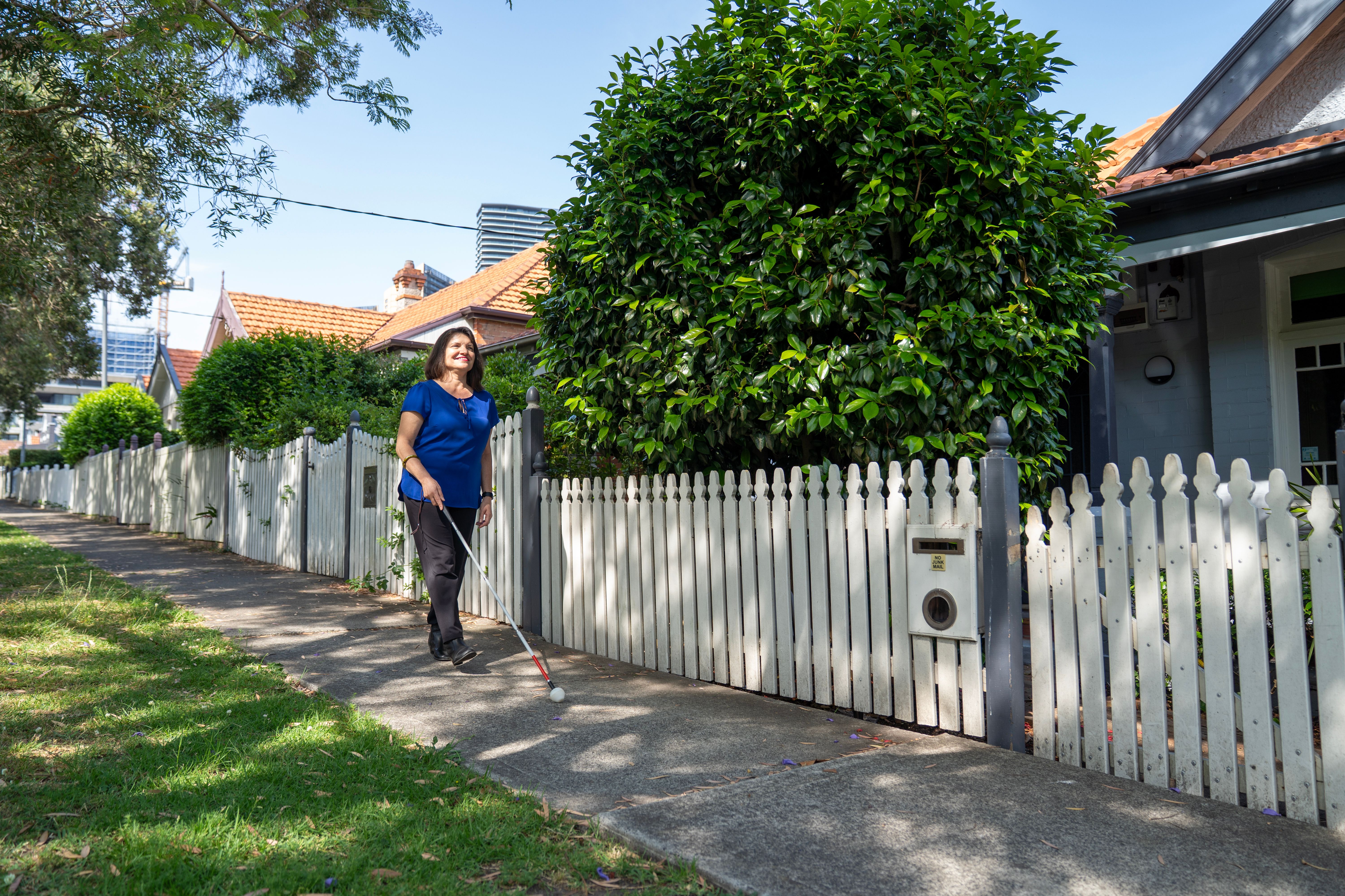 A person walking along the footpath with a white cane. 
