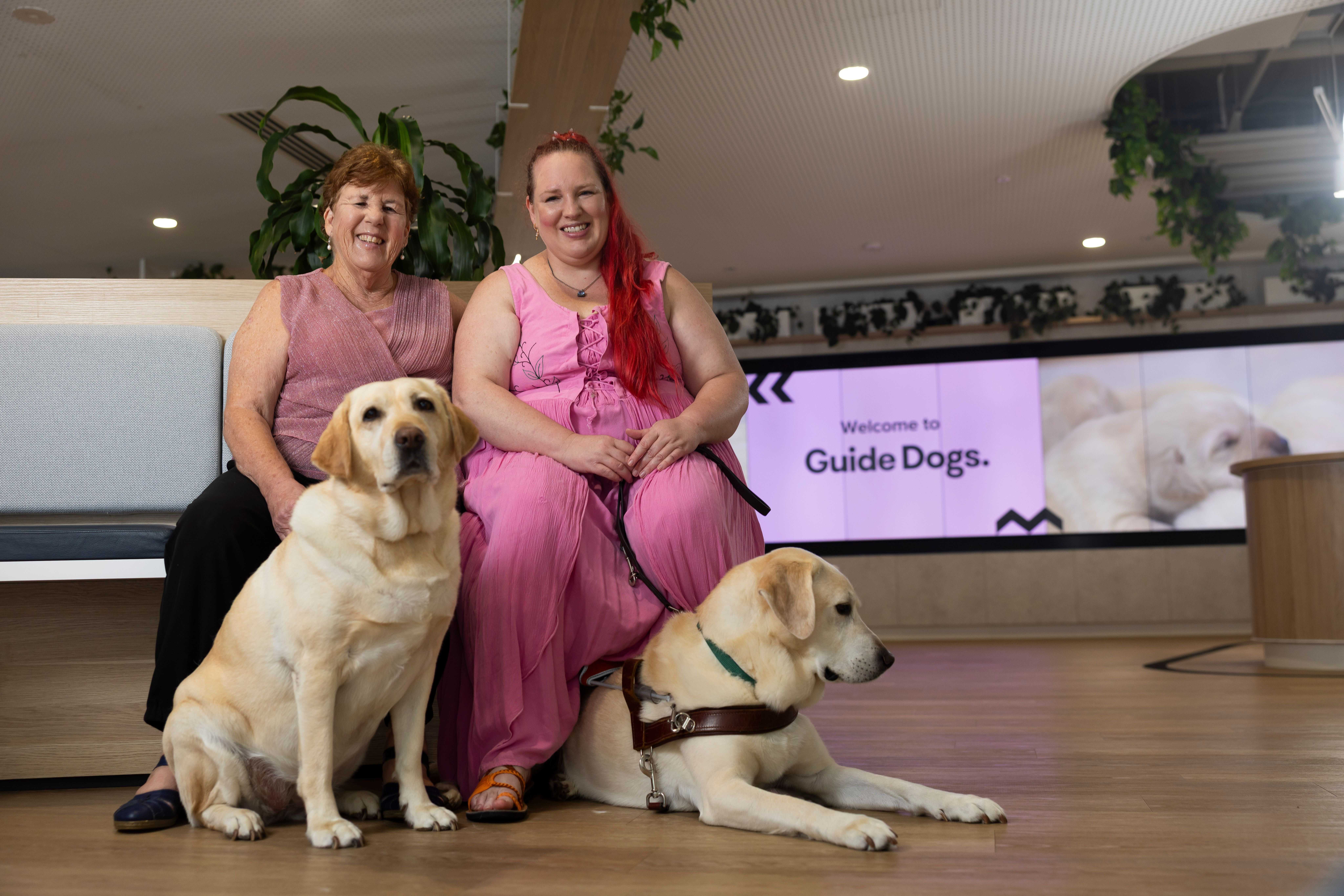 Two people sitting with their Guide Dogs.