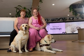 Two people sitting with their Guide Dogs.