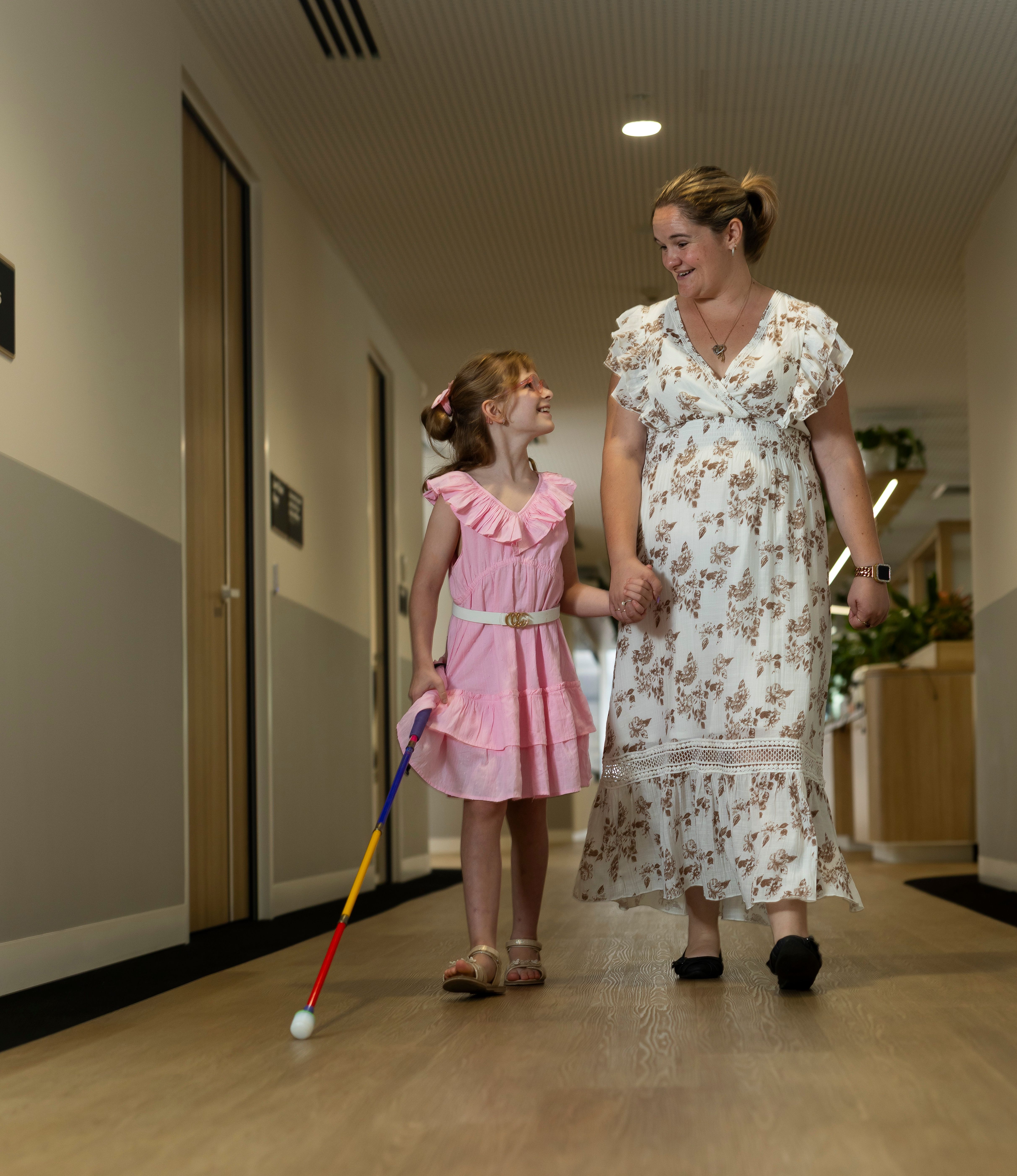 A mother walking with her daughter who is using a white cane.